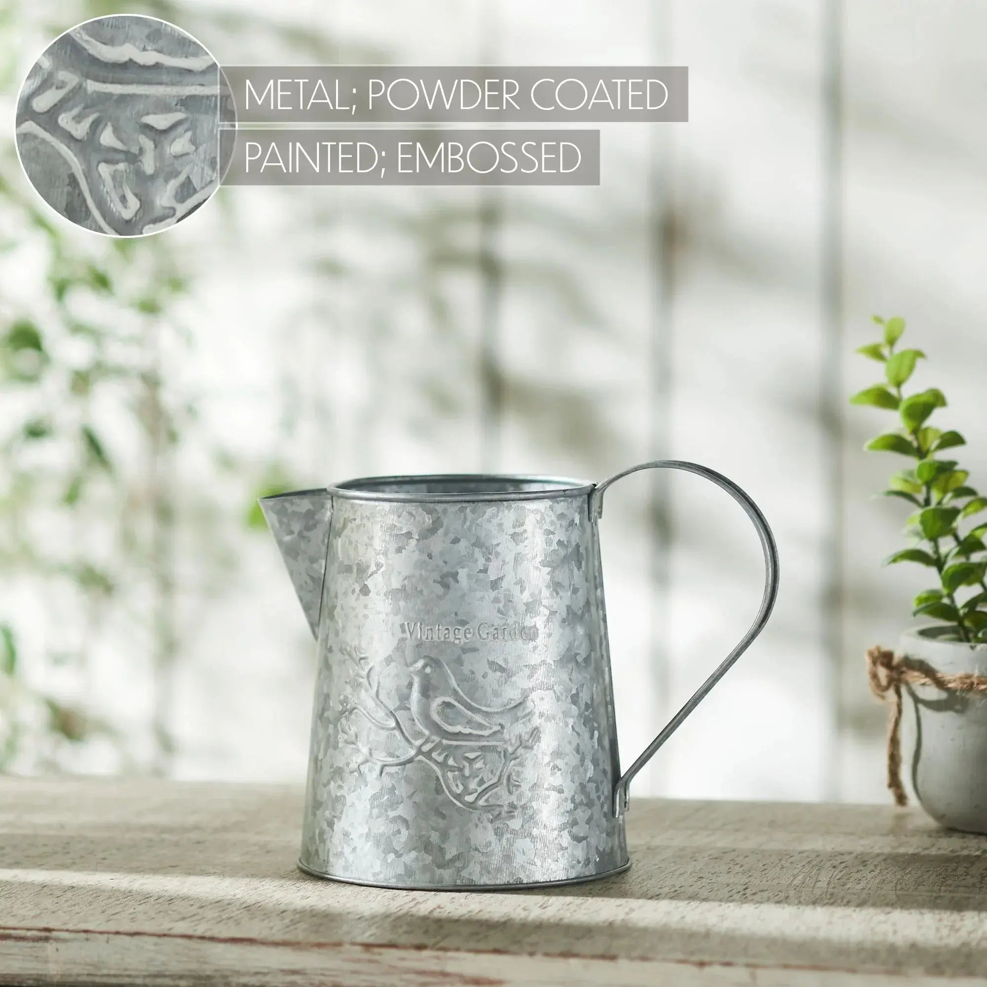 Metal watering can with embossed design on a wooden surface with a blurred natural background