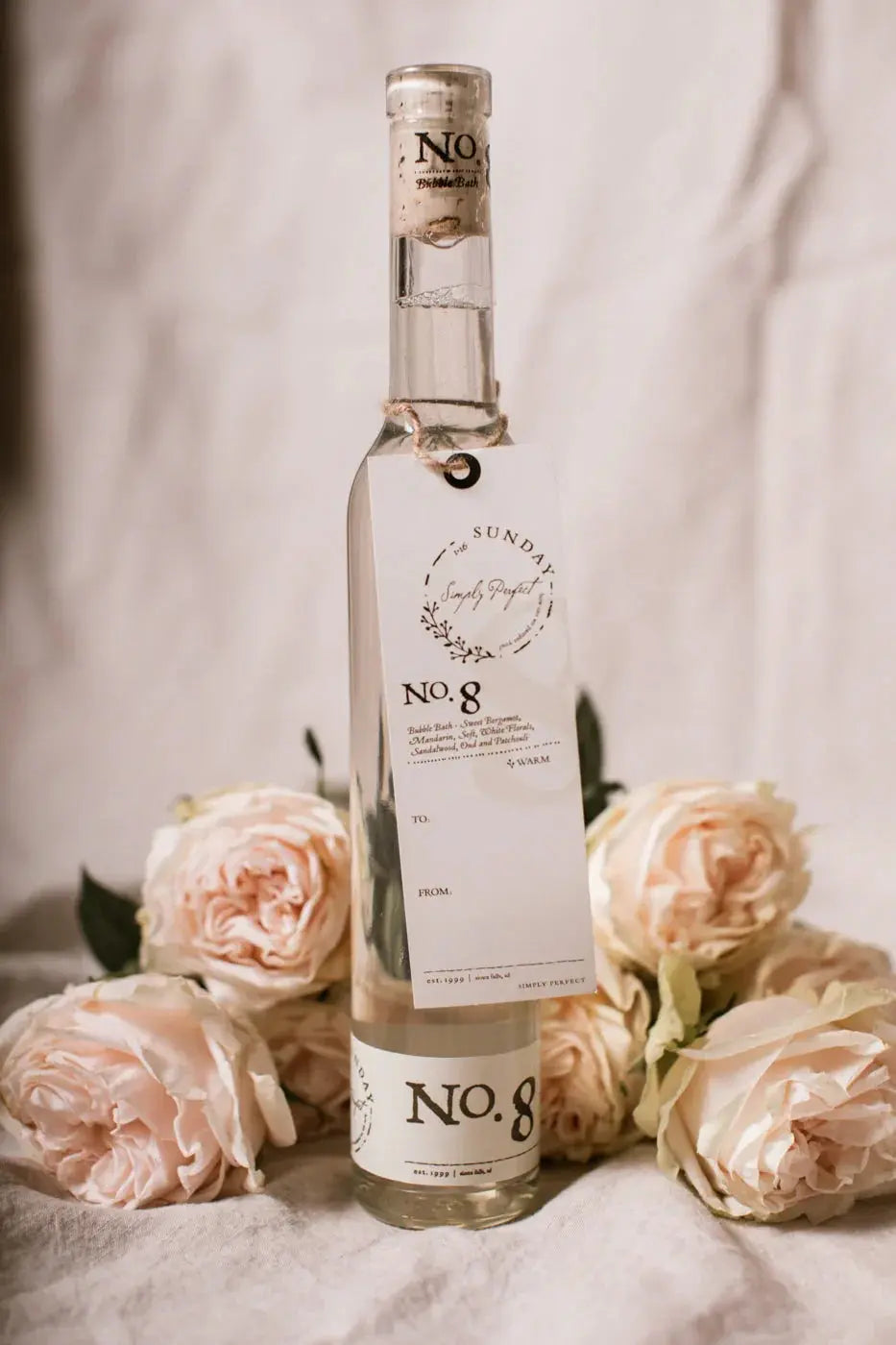 No. 8 bubble bath bottle with floral tag, surrounded by soft pink roses, cozy farmhouse bath essential