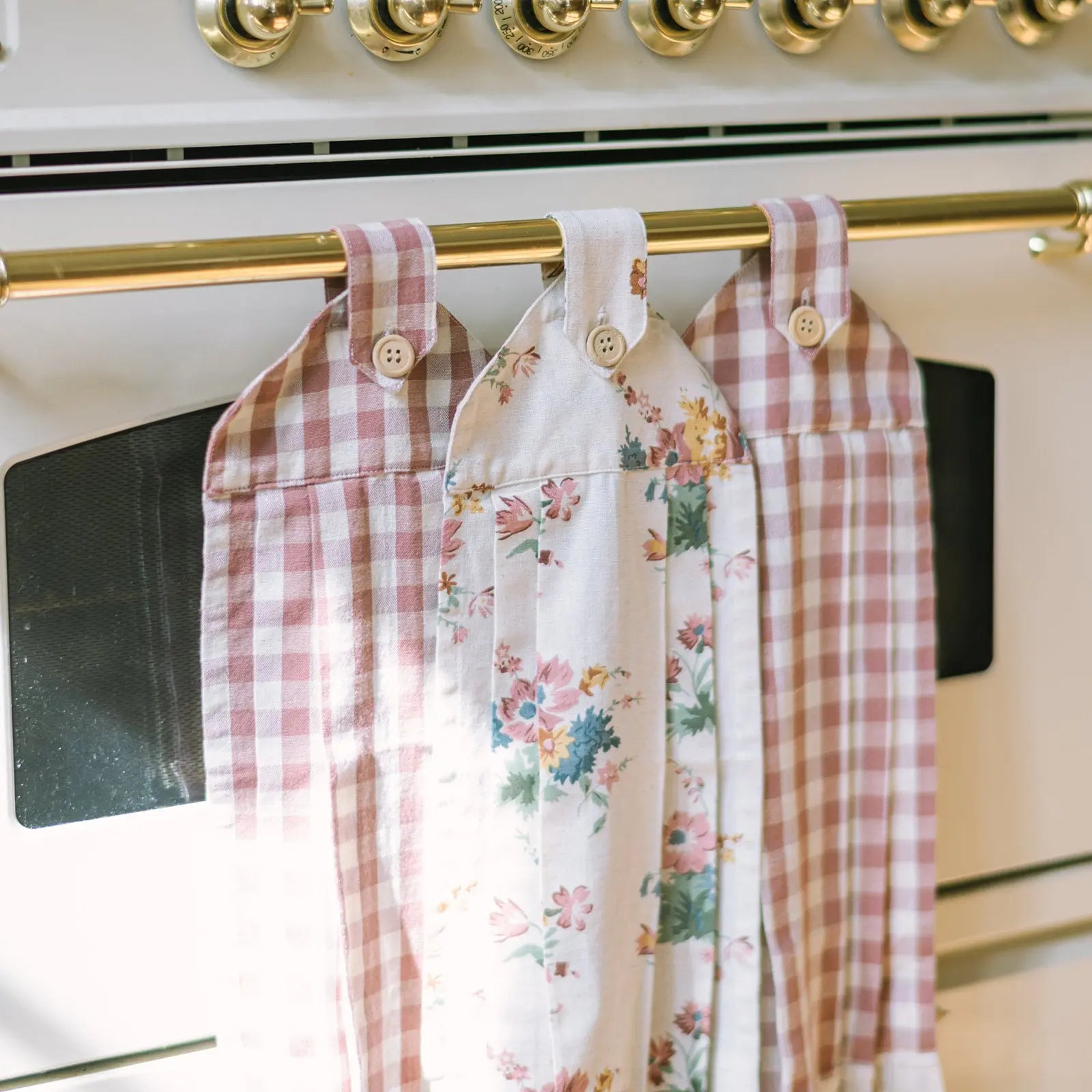 Two plaid shirts and one floral shirt hanging on a gold rod against a white stove background.