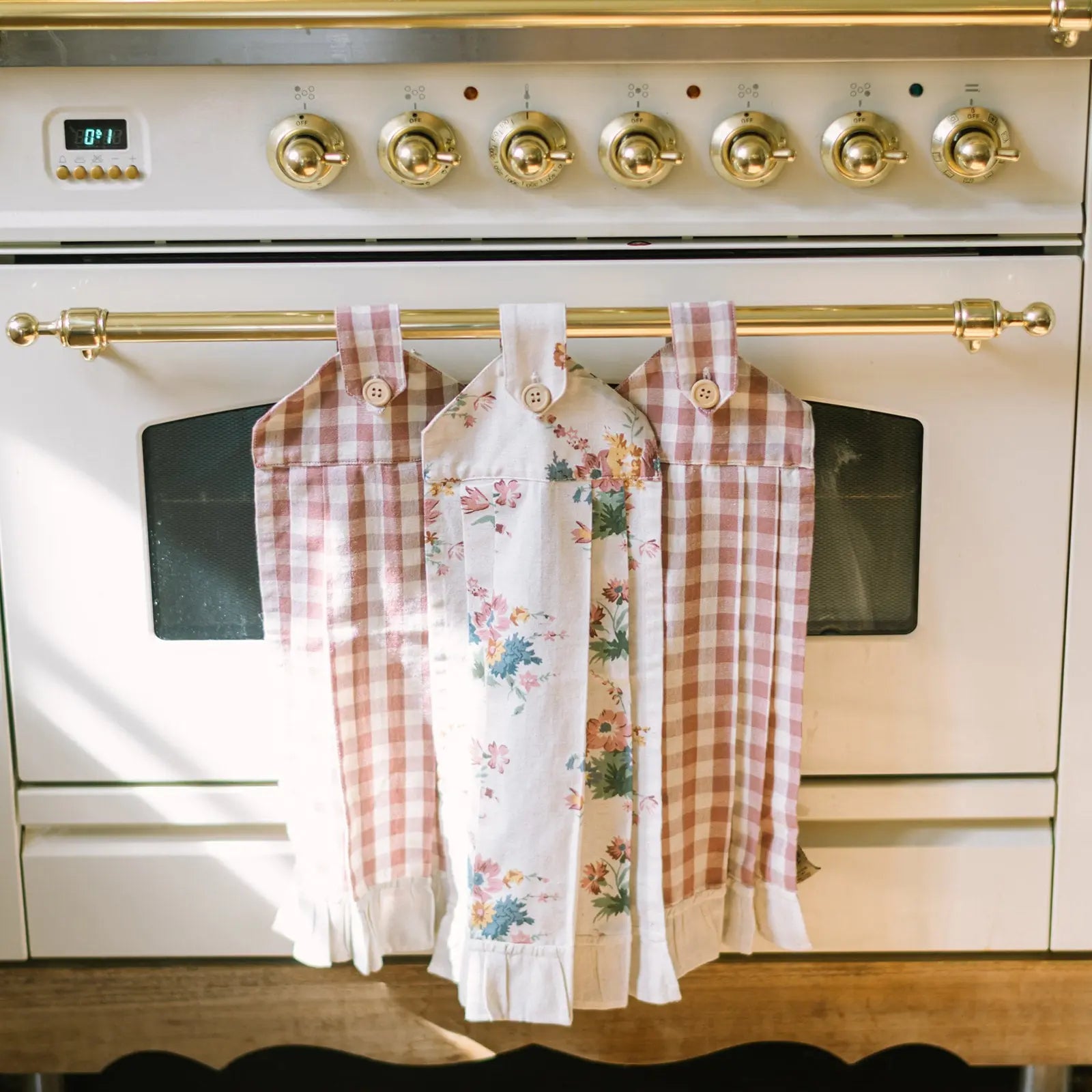 Three dishtowels hanging on a gold towel rack above a stove.