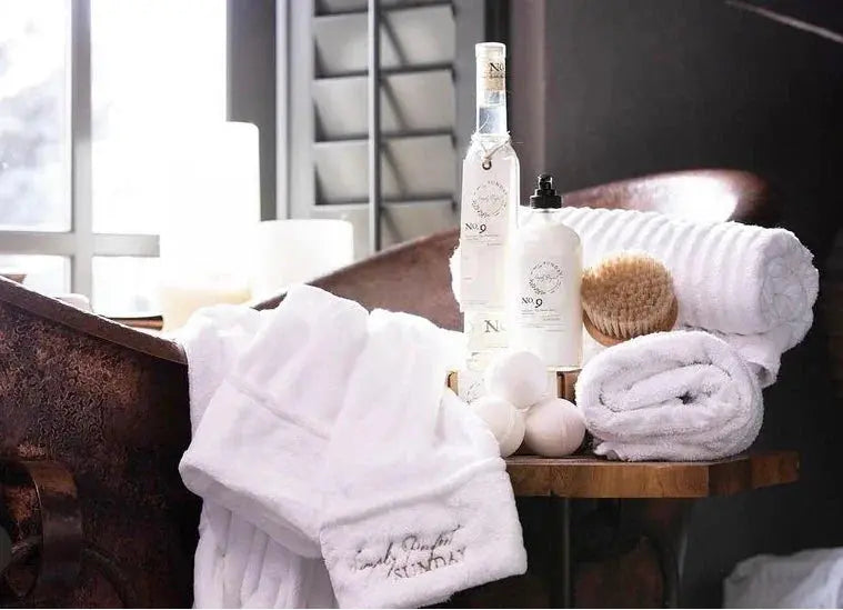 Cozy farmhouse bath setup with white towels, No. 9 bath products, and wooden brush near rustic tub