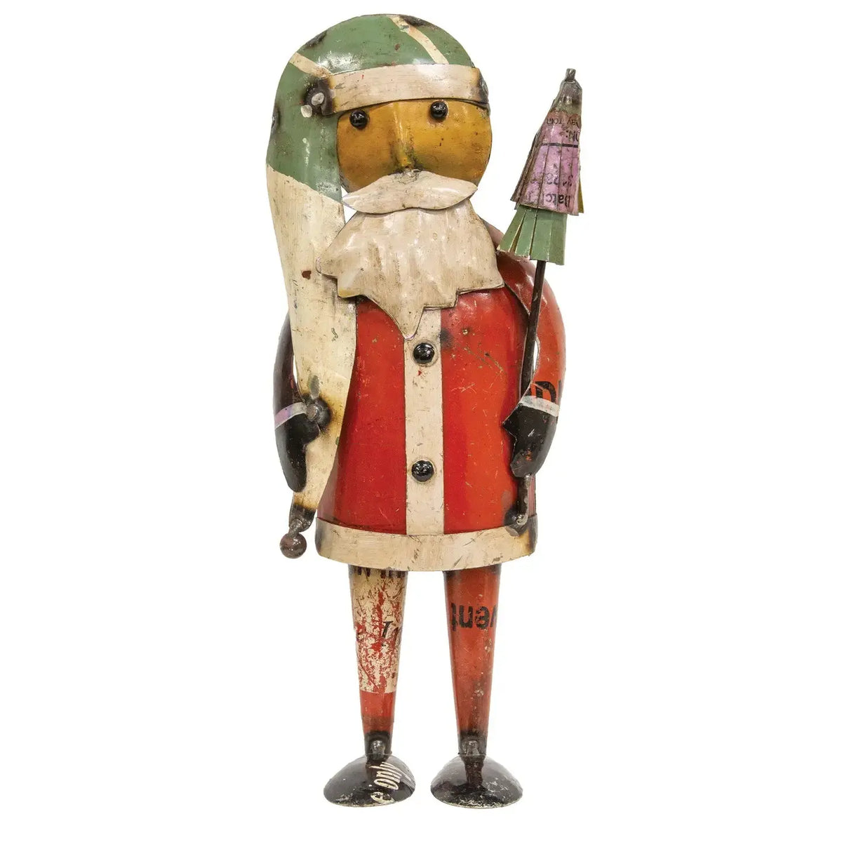 A vintage tin Santa Claus figurine with a weathered red, green, and cream painted finish, holding a small Christmas tree, isolated on a white background.