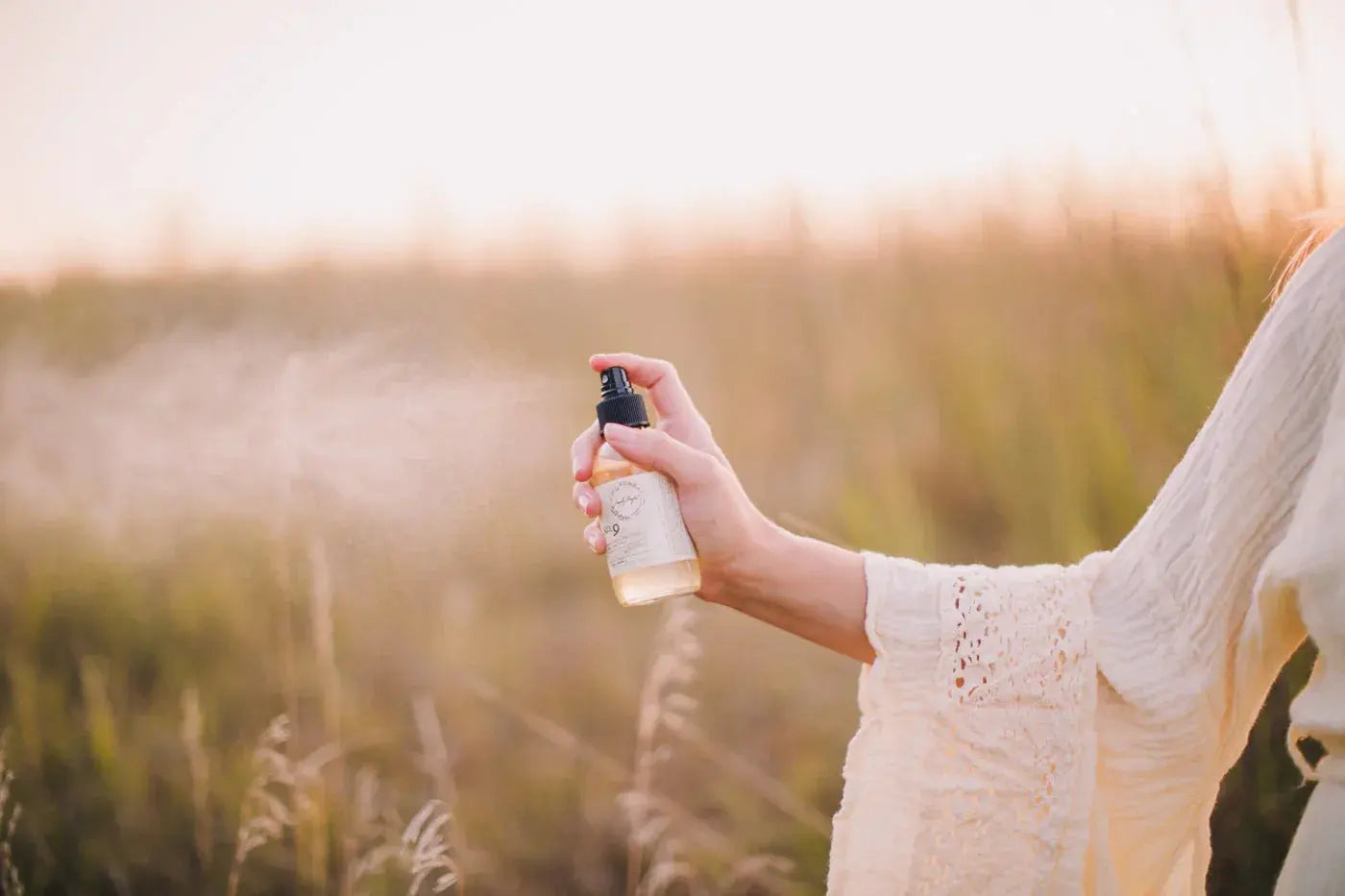 Woman spraying linen spray in golden field, cozy farmhouse home fragrance for peaceful living spaces