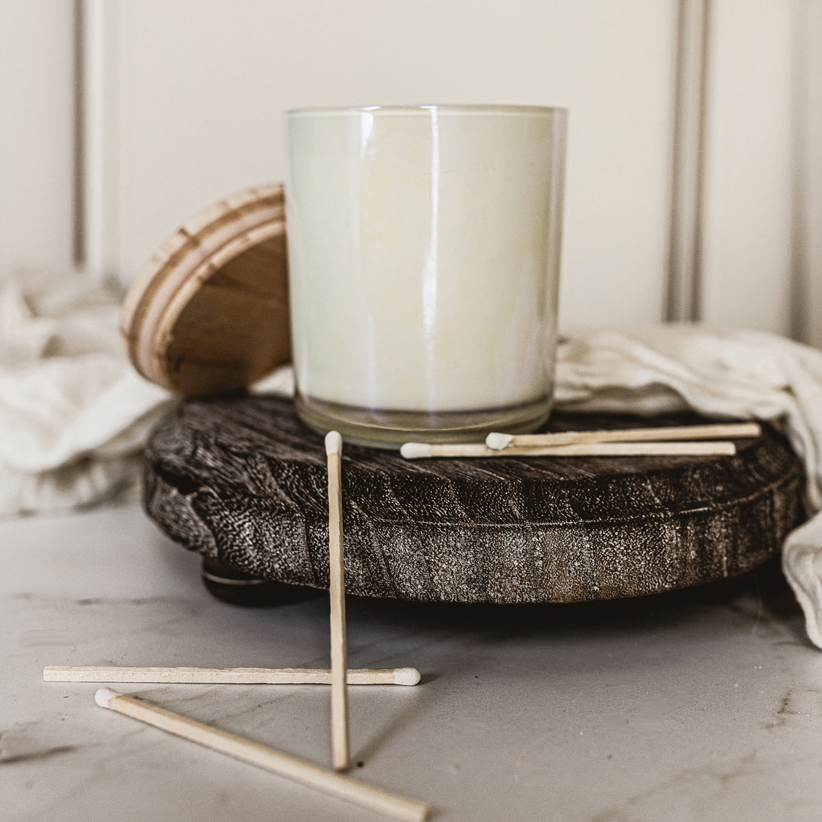 Candle on a wooden coaster with matches on a light surface