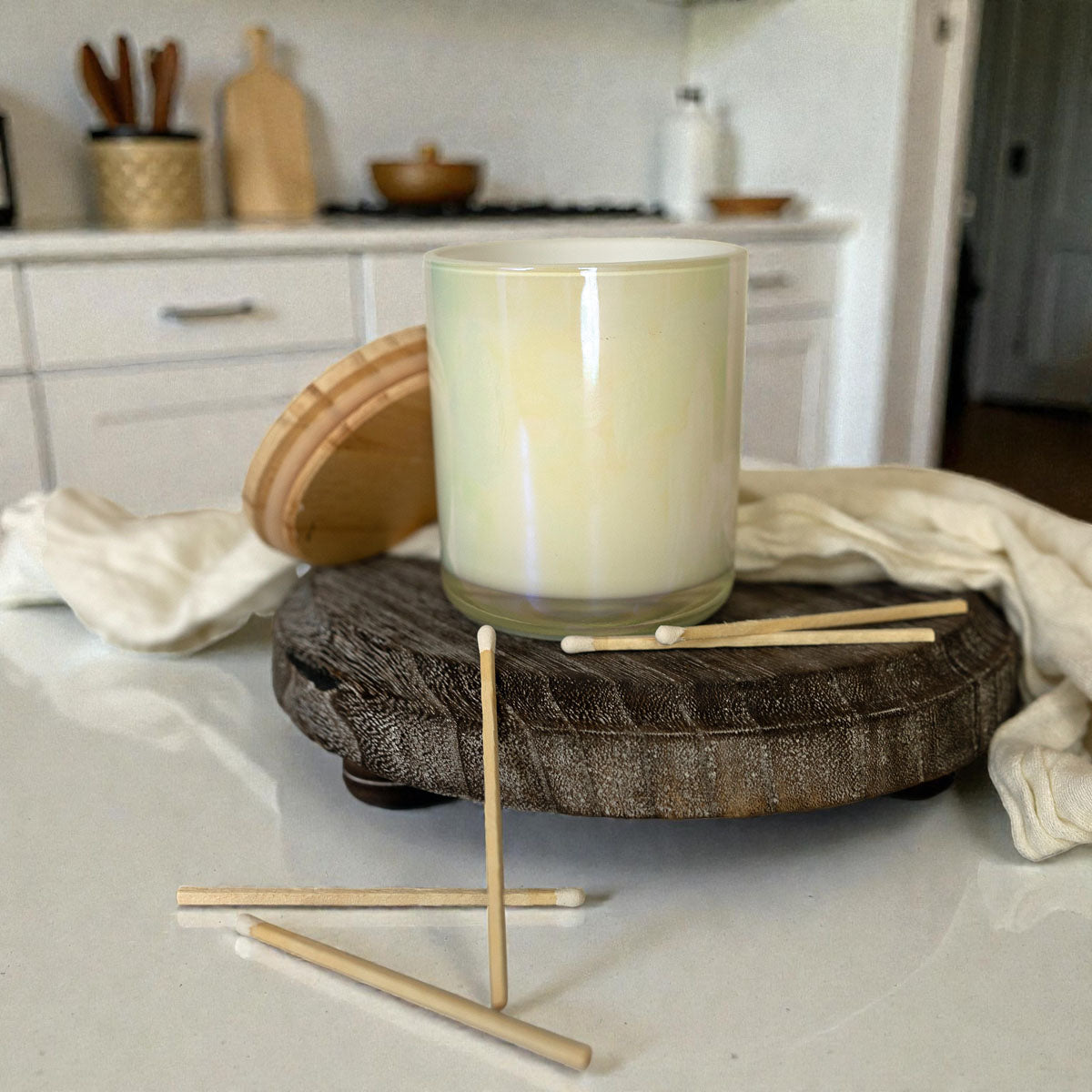 Candle on a wooden coaster with kitchen utensils in the background