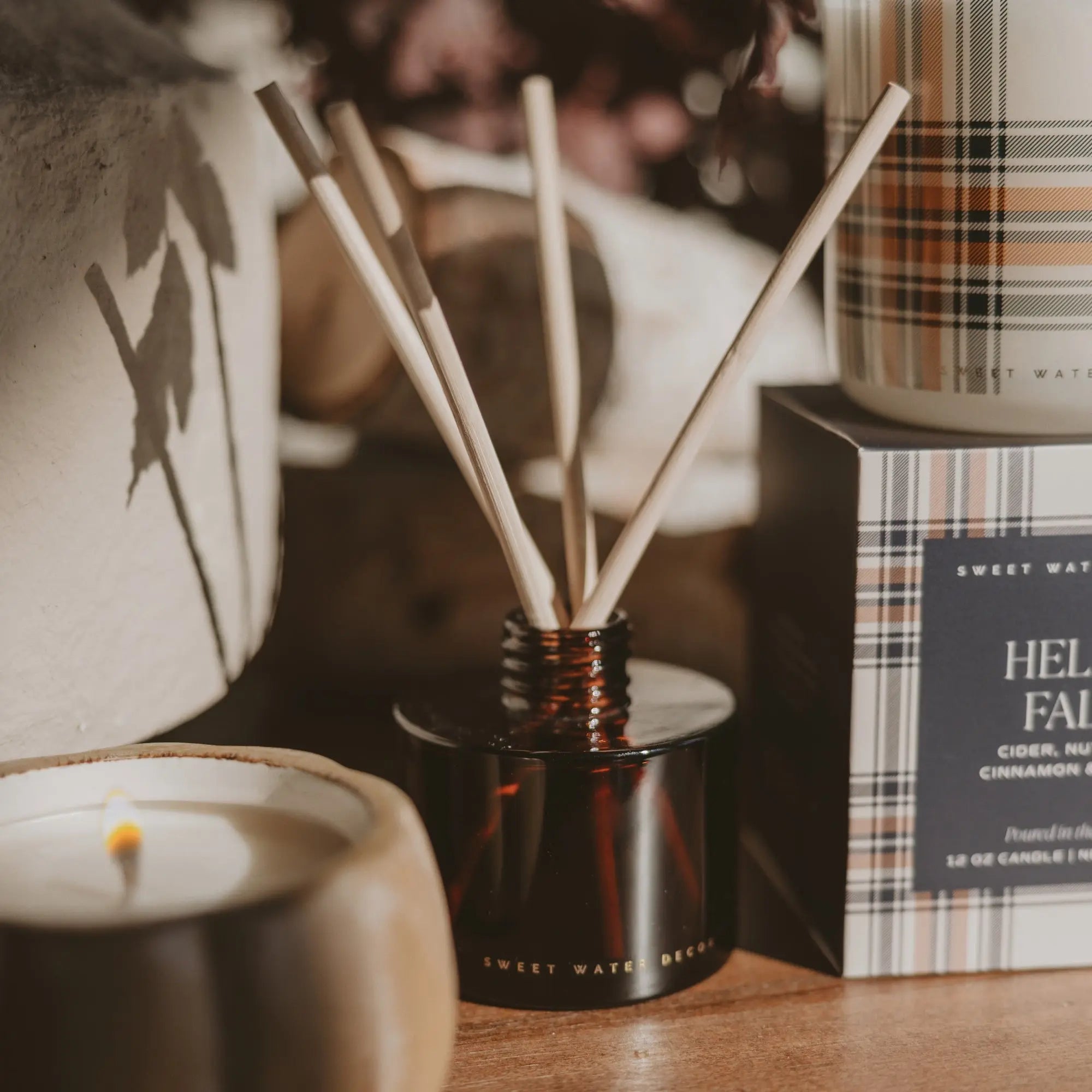 A diffuser with sticks, a candle, and a box on a wooden surface.