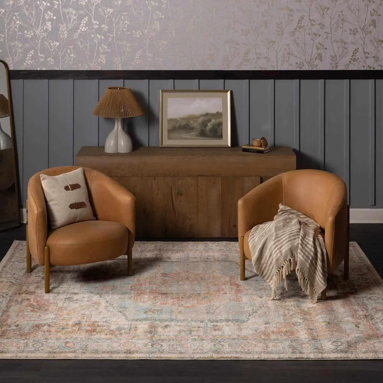 Cozy farmhouse living room with leather armchairs, vintage rug, wooden console, and floral wallpaper