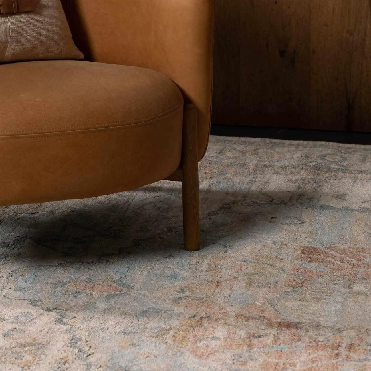 Cozy farmhouse rug with vintage pattern under a brown leather armchair, perfect for cottage style living rooms.
