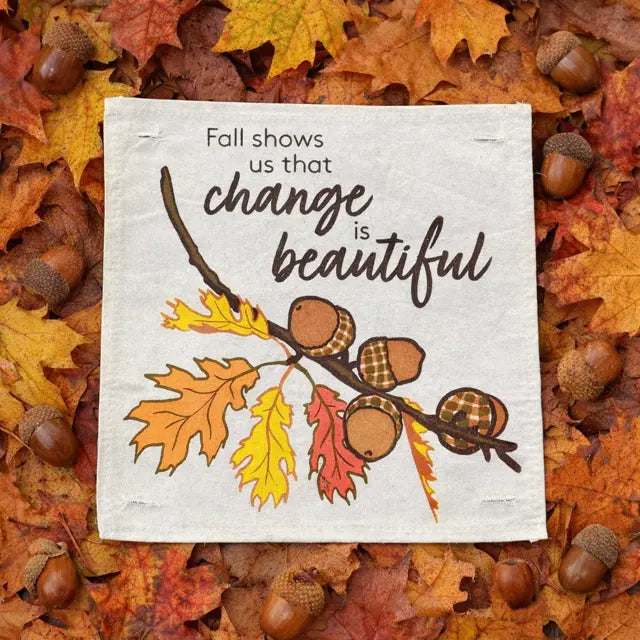 Decorative sign with autumn leaves and acorns on a bed of fall leaves.