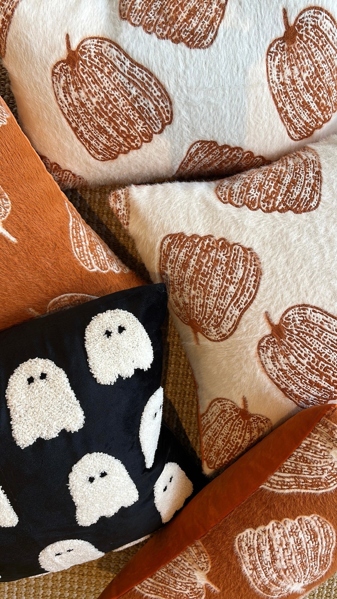Decorative pillows with pumpkin and ghost patterns on a textured surface.