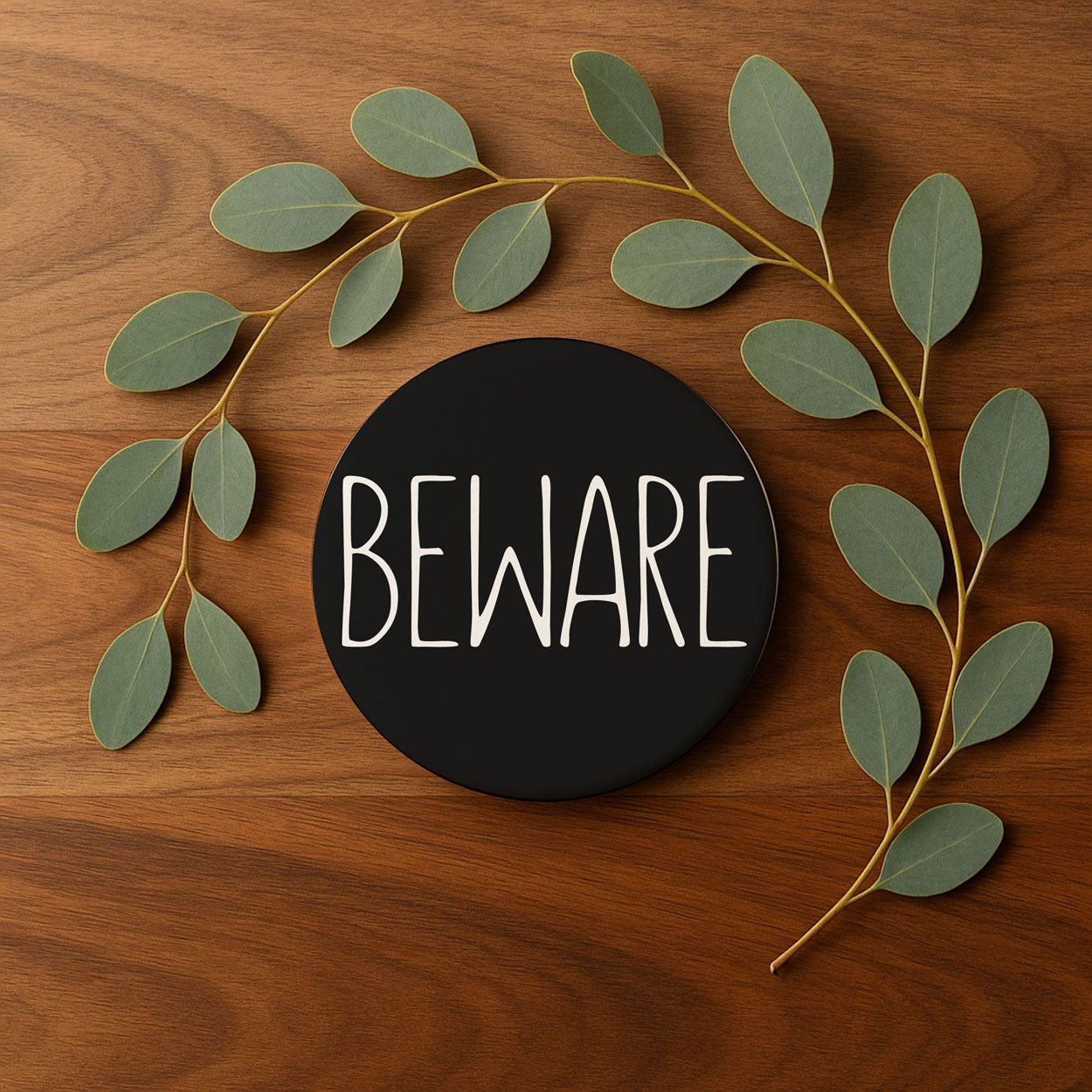 Decorative sign with 'BEWARE' text surrounded by green leaves on a wooden background