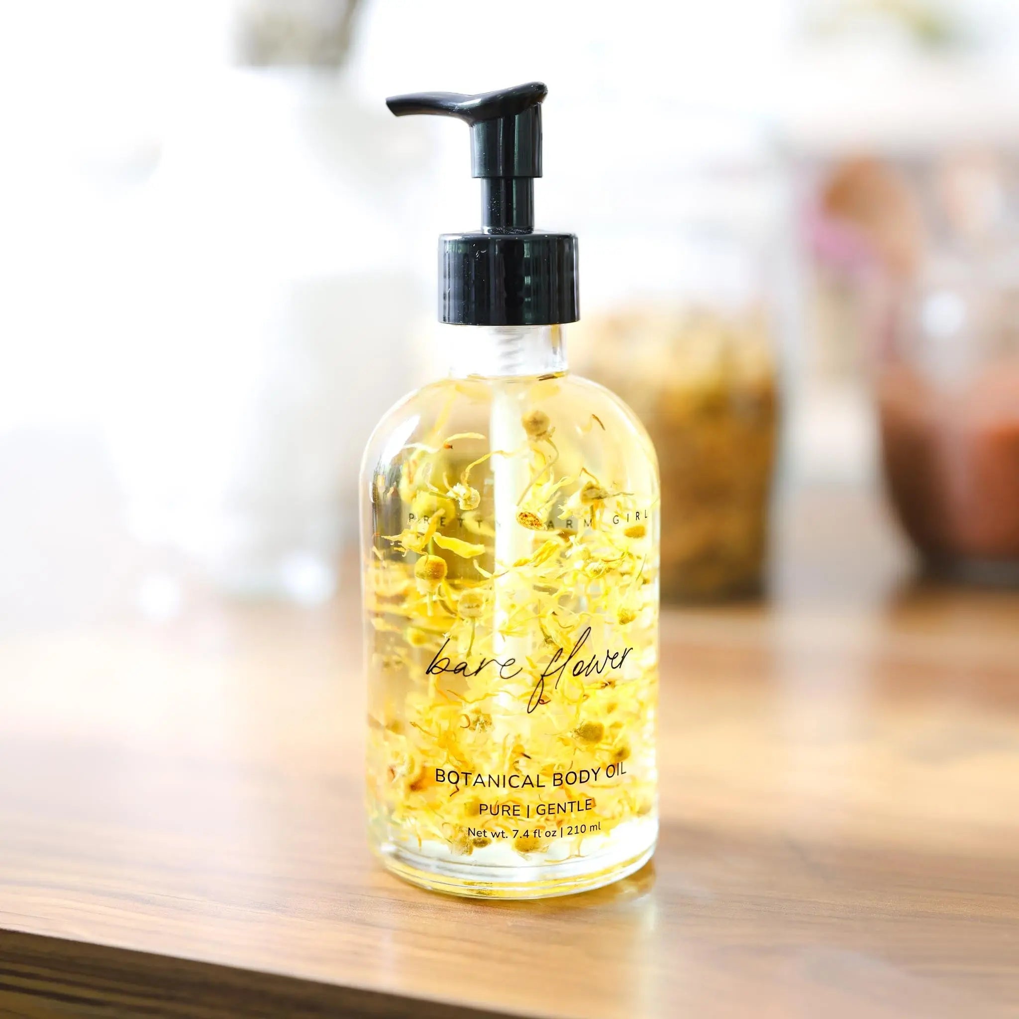 Bottle of Botanical Body Oil with text Bare Flower. Sitting on a wooden table.