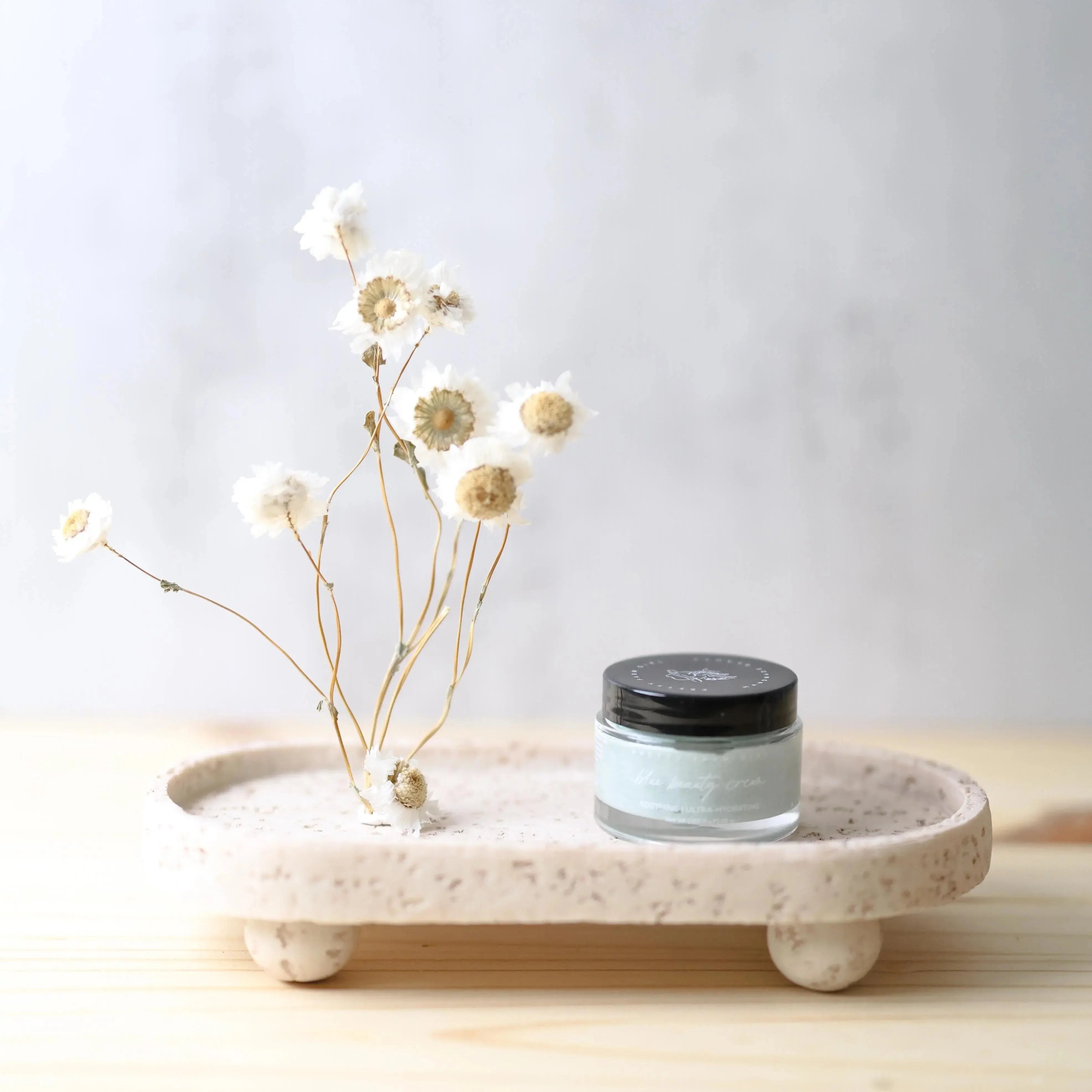 Soothing ultra-hydrating beauty cream with dried white flowers on a speckled ceramic tray, farmhouse decor