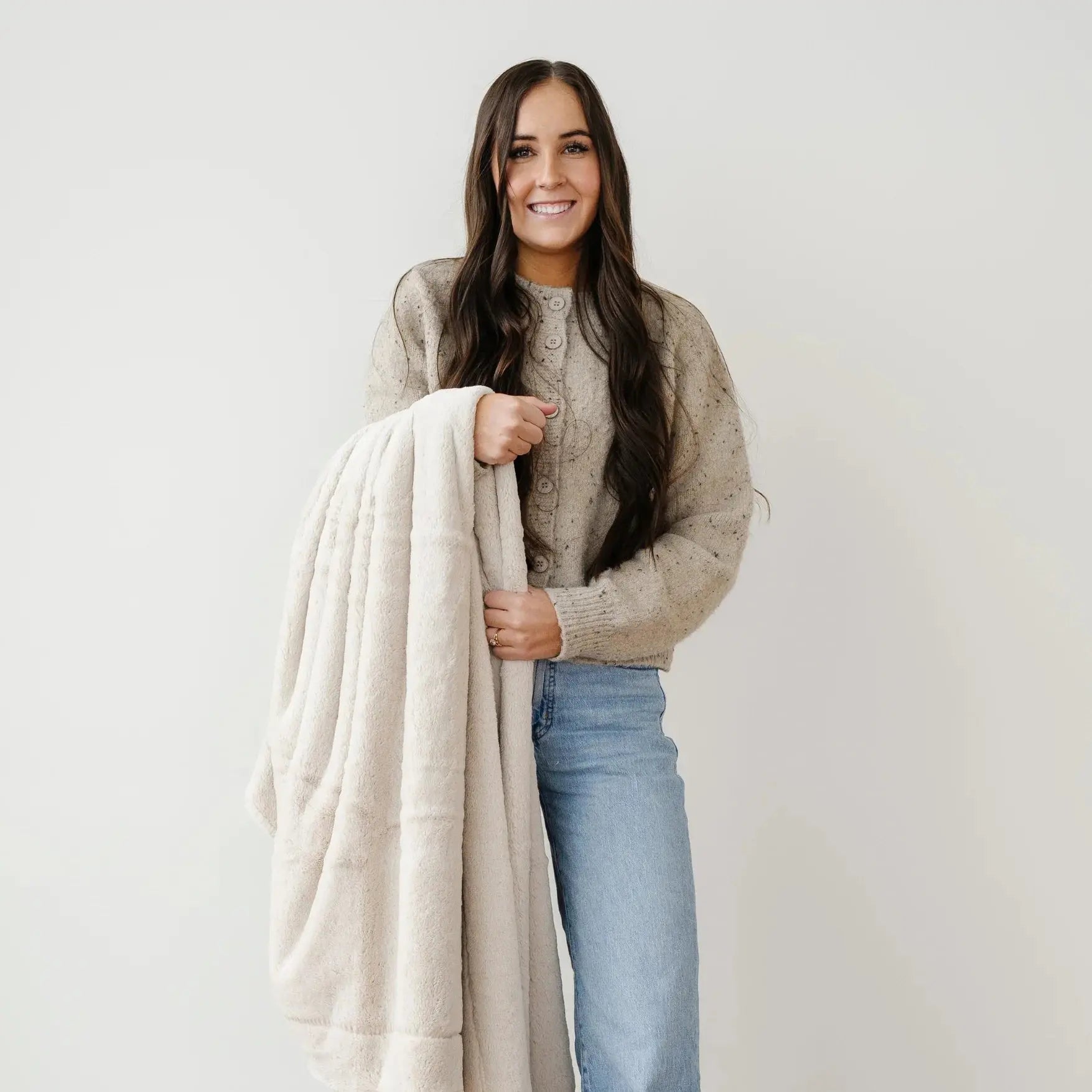 Woman holding a beige blanket against a plain background