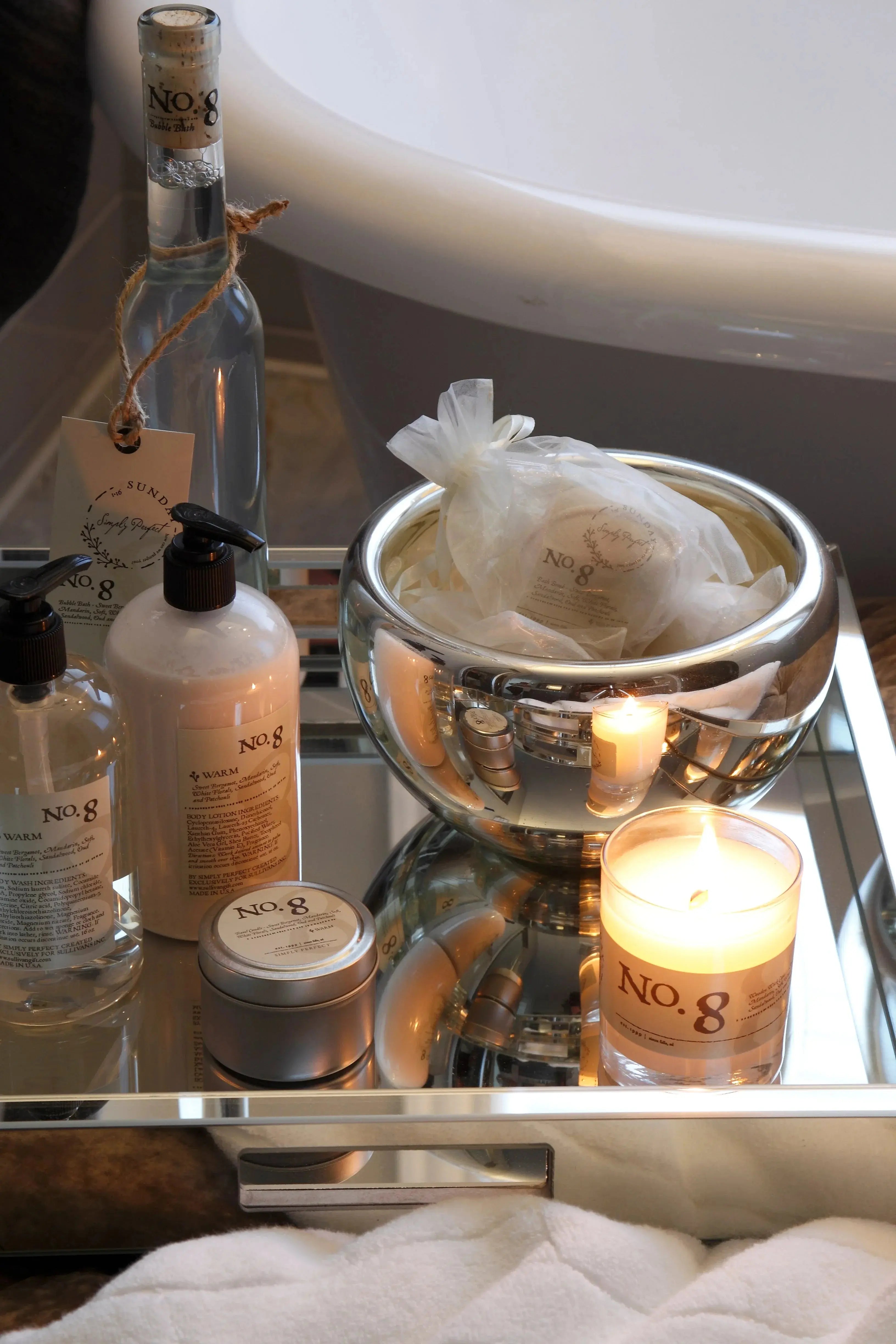 Cozy No. 8 bath set with candles, lotions, and bath bombs on mirrored tray near bathtub, farmhouse spa decor