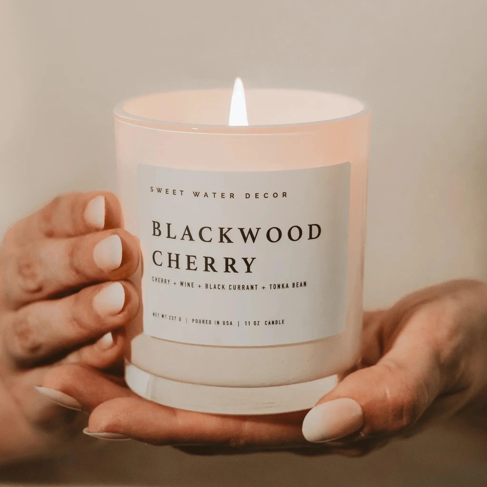 Blackwood Cherry scented candle in frosted glass, held gently, perfect for cozy farmhouse decor and relaxing ambiance