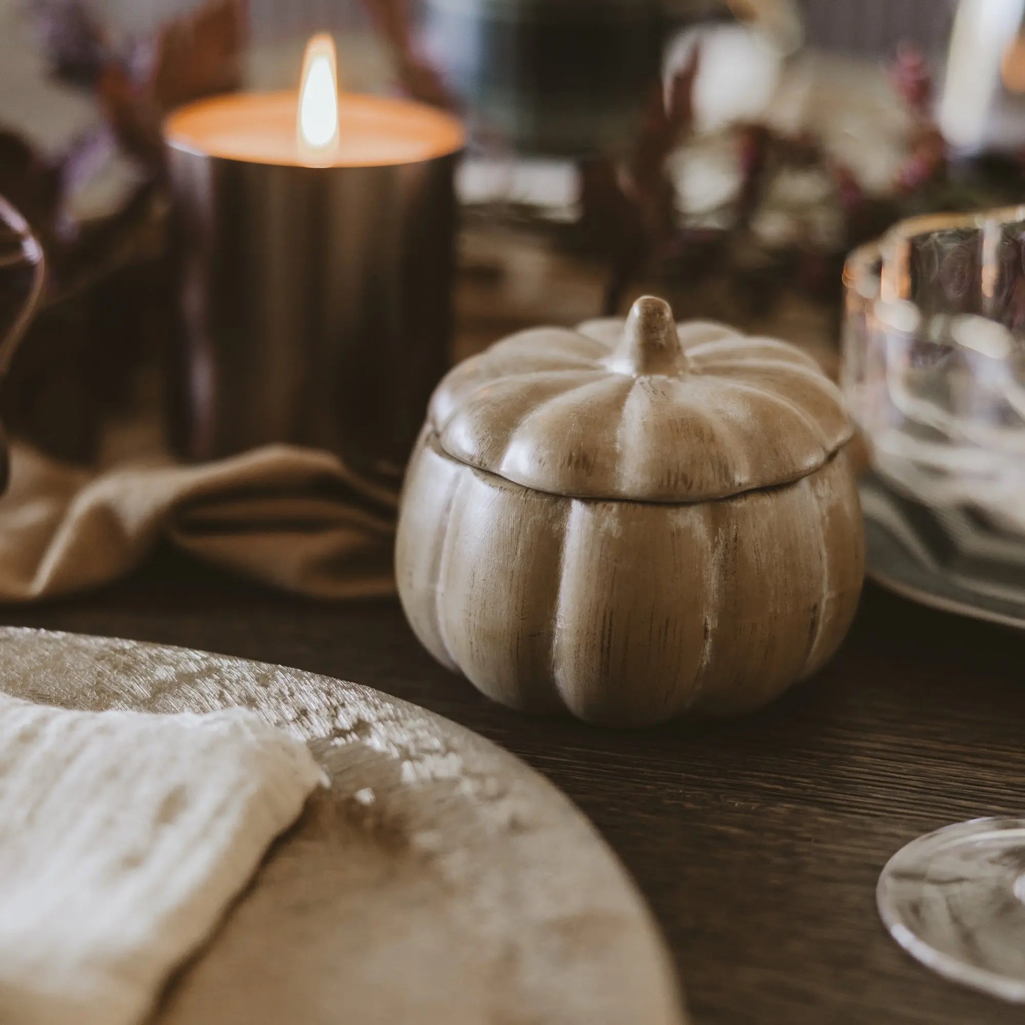 Decorative pumpkin-shaped container on a wooden surface with candles in the background
