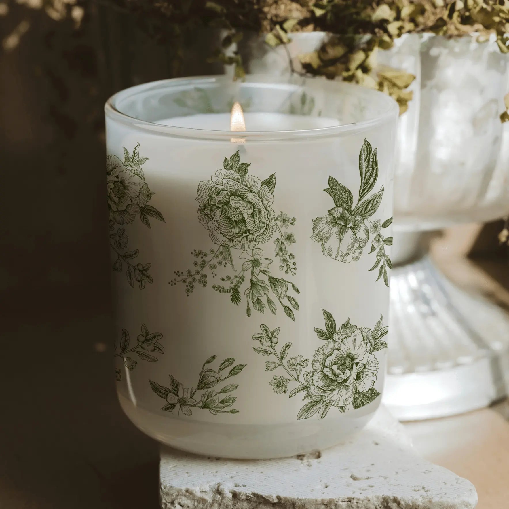 Lit floral candle in frosted glass jar, farmhouse decor with green botanical print, cozy cottage style ambiance