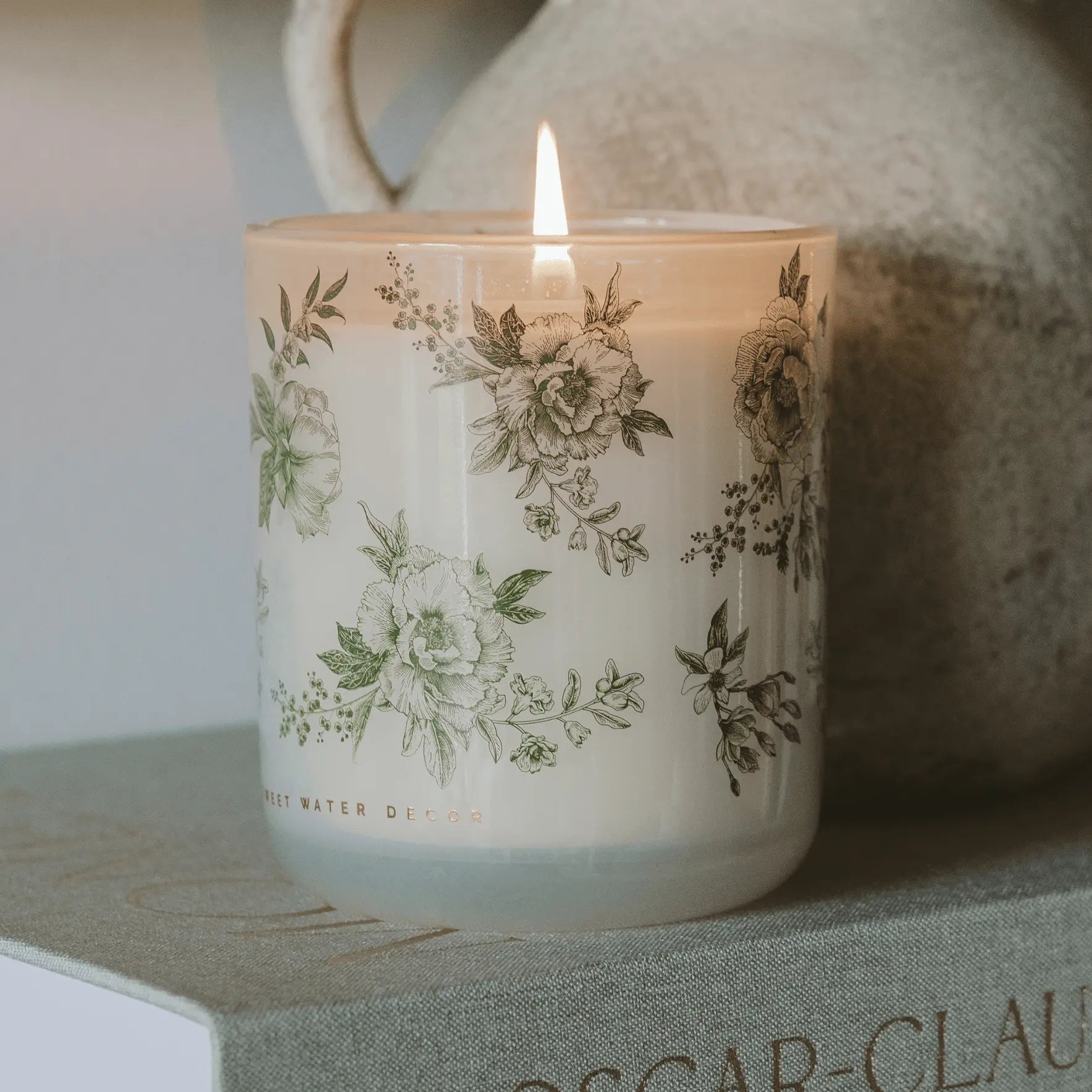 Lit floral candle in vintage glass jar, cozy farmhouse decor with botanical print, perfect for warm home ambiance
