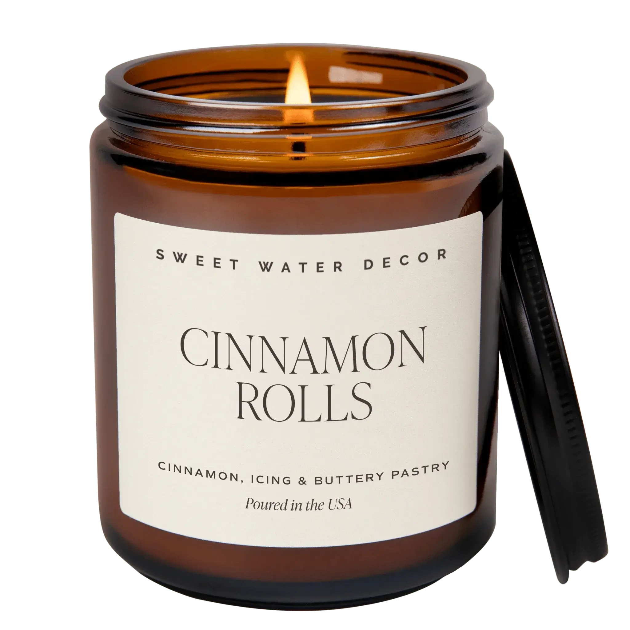 Candle in an amber jar labeled 'Cinnamon Rolls' by Sweet Water Decor on a white background