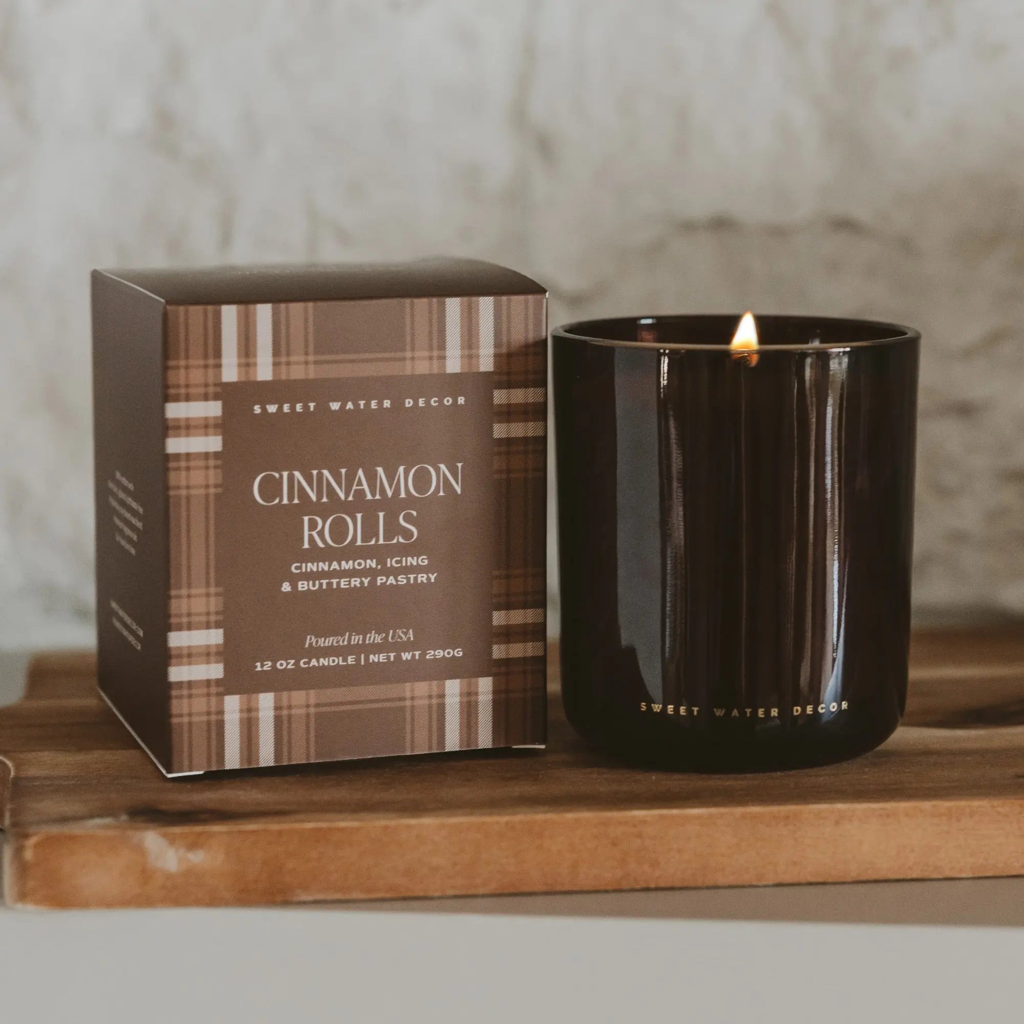 Candle and packaging with 'Cinnamon Rolls' description on a wooden surface.