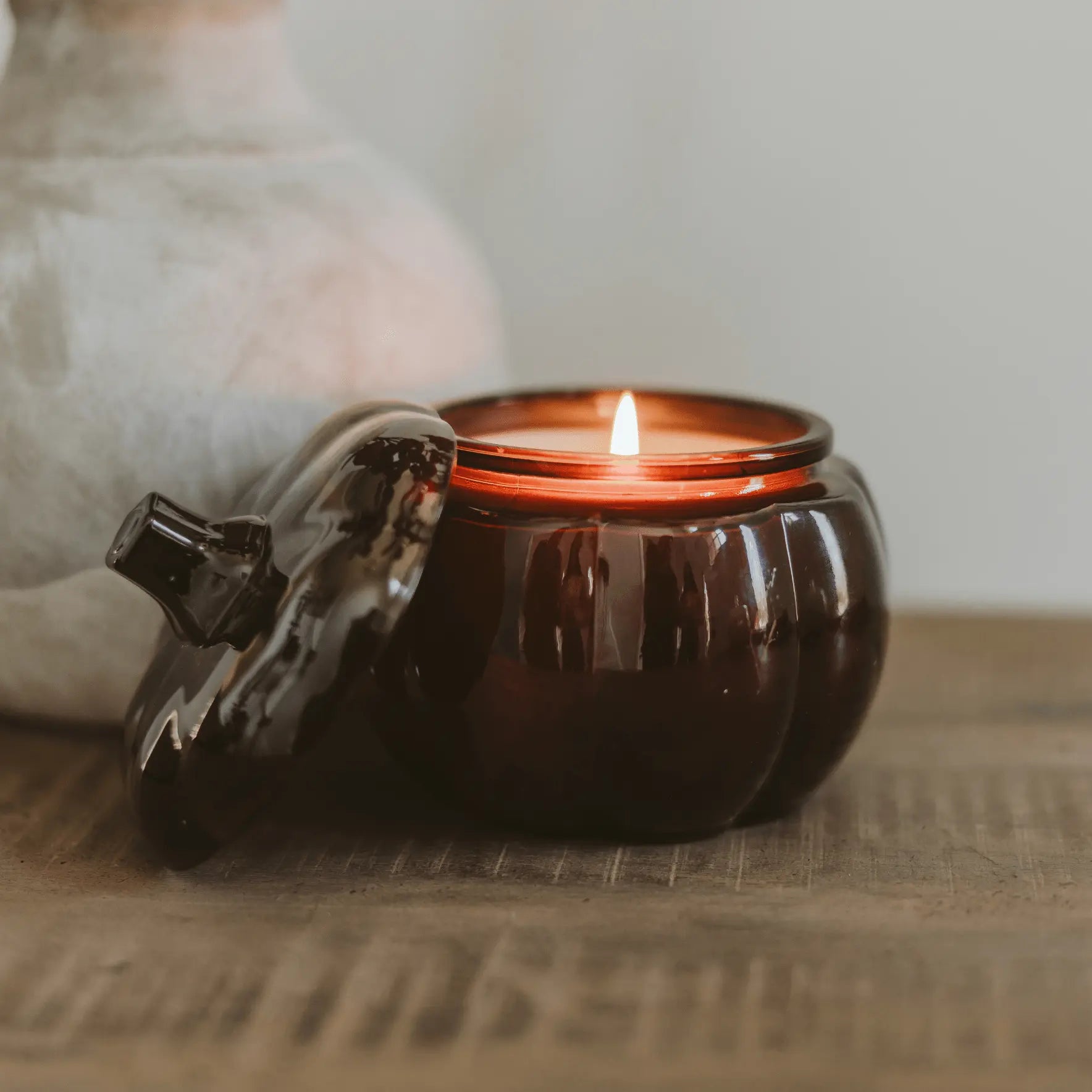 Candle in a pumpkin-shaped container on a wooden surface with a blurred background