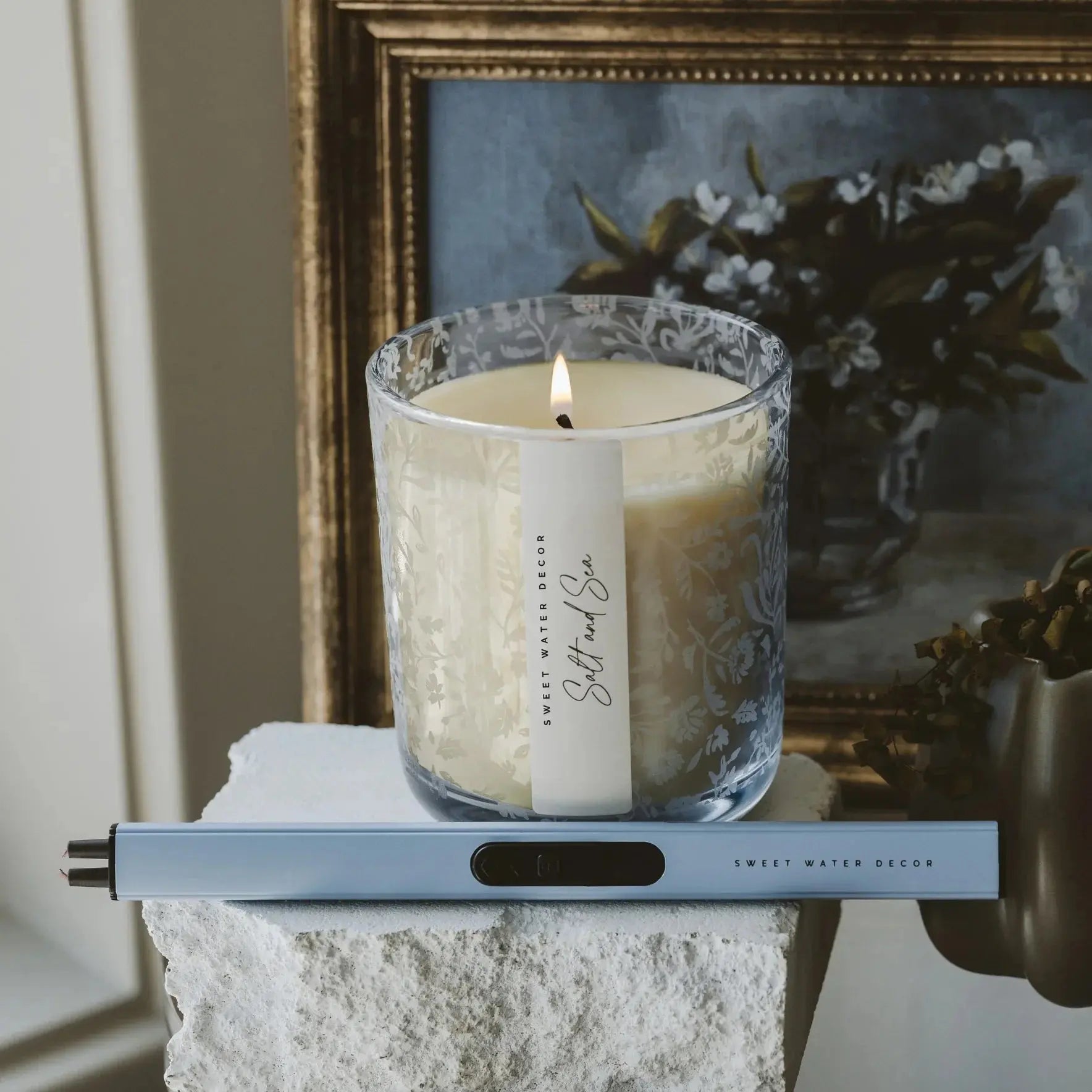 Lit 'Salt and Sea' candle in floral glass jar, cozy farmhouse decor with framed art and stone base