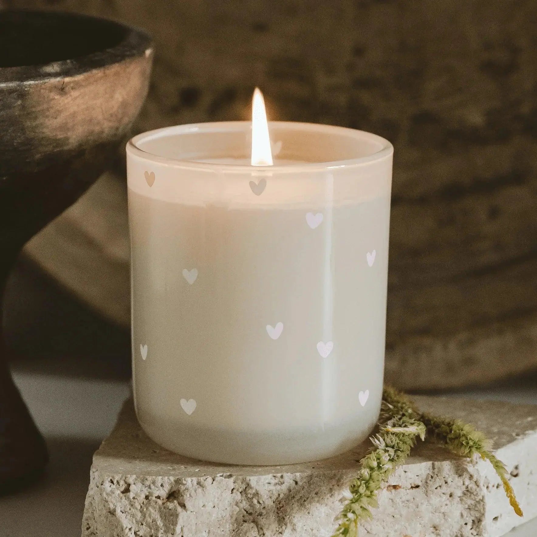 Lit heart-patterned candle in frosted glass, cozy farmhouse decor with moss and stone