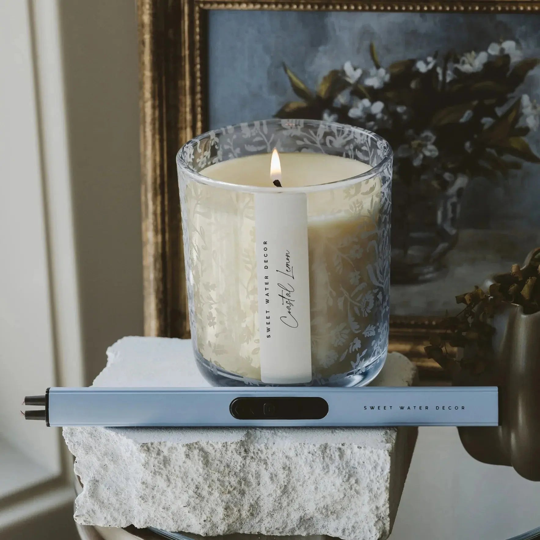 Cozy Coastal Lemon candle in floral glass jar, lit on stone block with decor, perfect for farmhouse home ambiance.