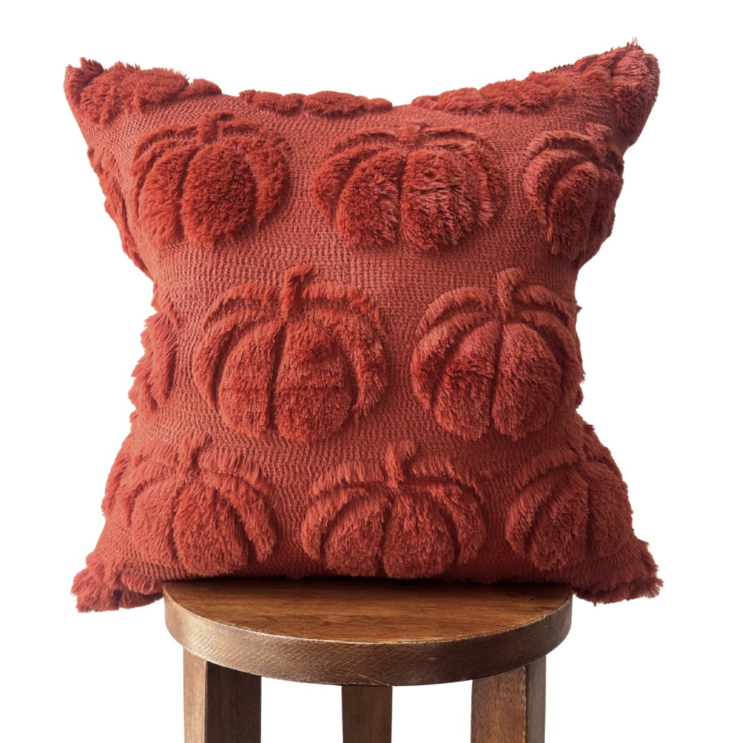 Red textured pillow with pumpkin pattern on a wooden stool against a white background