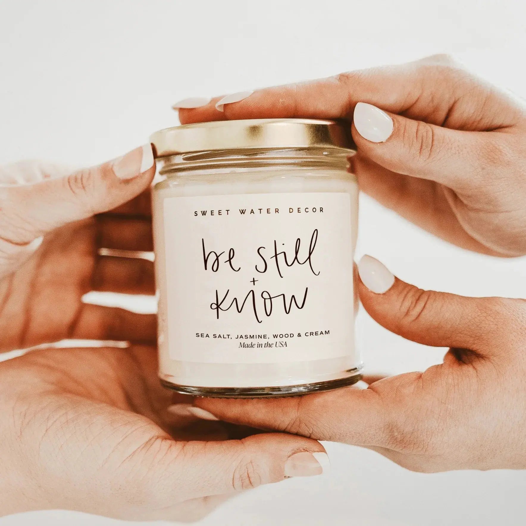 Be Still + Know candle with sea salt jasmine scent, cozy home decor, held in hands with gold lid