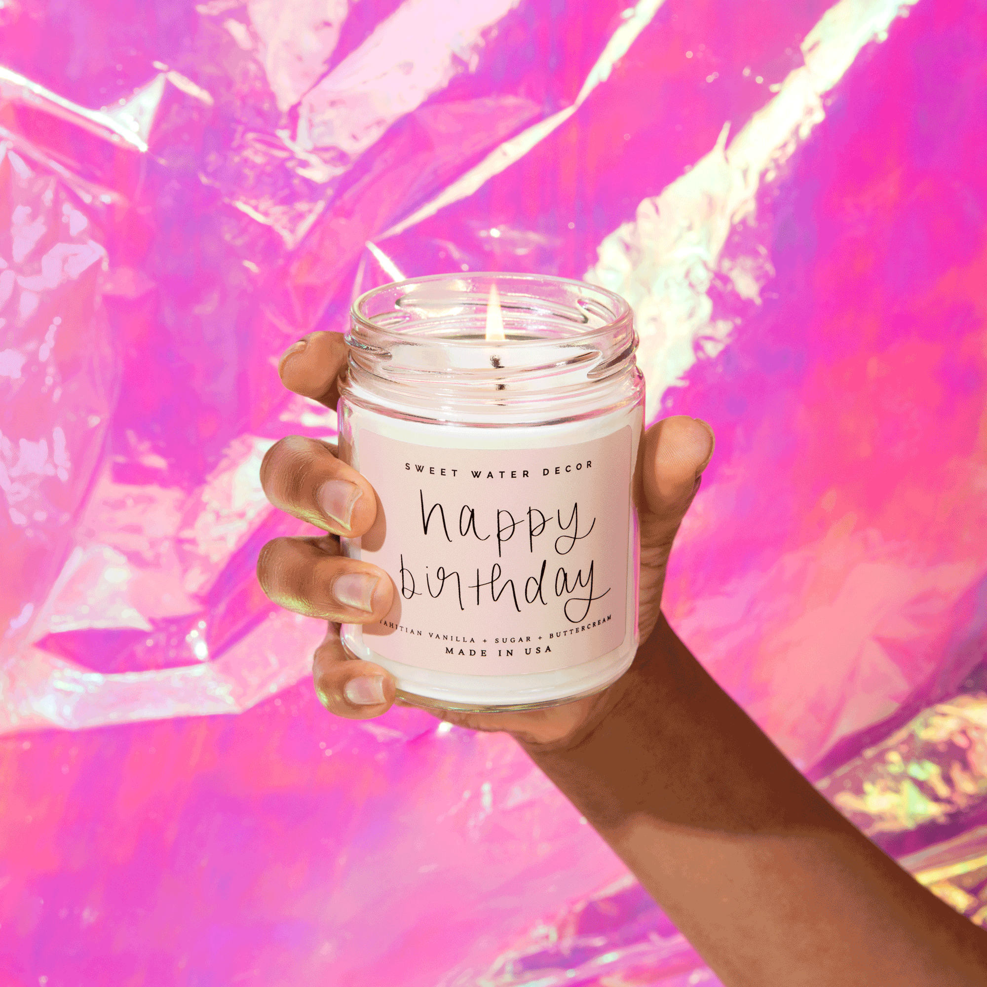 Hand holding lit 'Happy Birthday' candle with vanilla sugar buttercream scent, cozy home decor gift