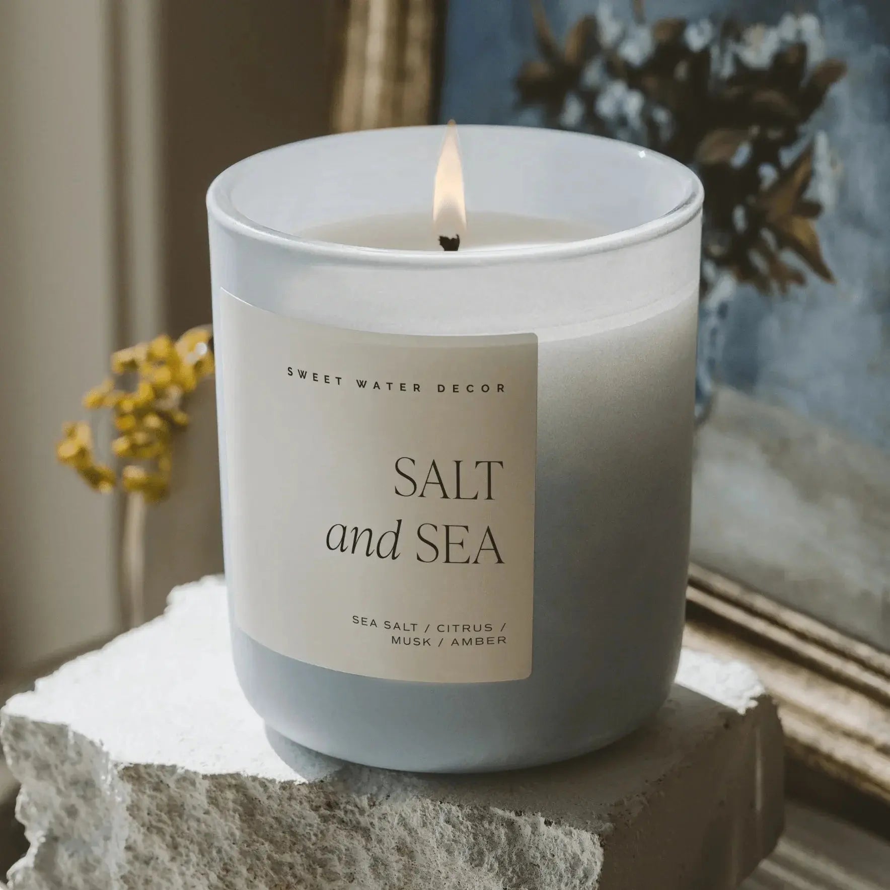 Salt and Sea scented candle in frosted glass, lit, on stone pedestal for cozy farmhouse decor