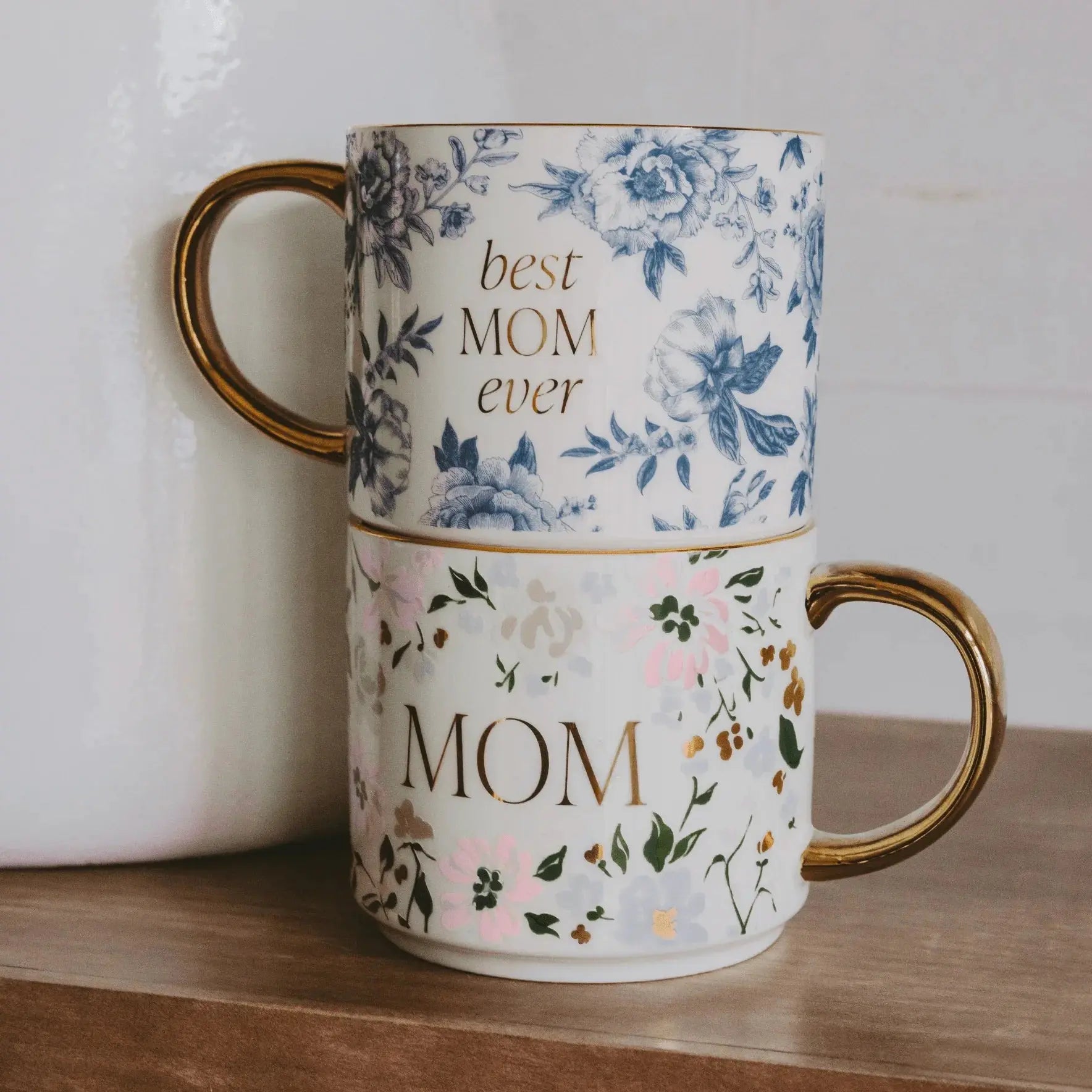 Two floral ceramic mugs with gold handles, one saying 'best MOM ever', ideal for cozy home decor or thoughtful gifts.