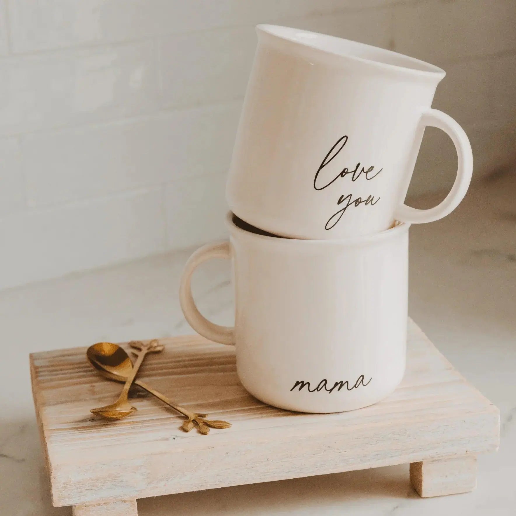 White ceramic mugs with 'love you' and 'mama' script, stacked on rustic wood tray with gold spoons, farmhouse kitchen decor