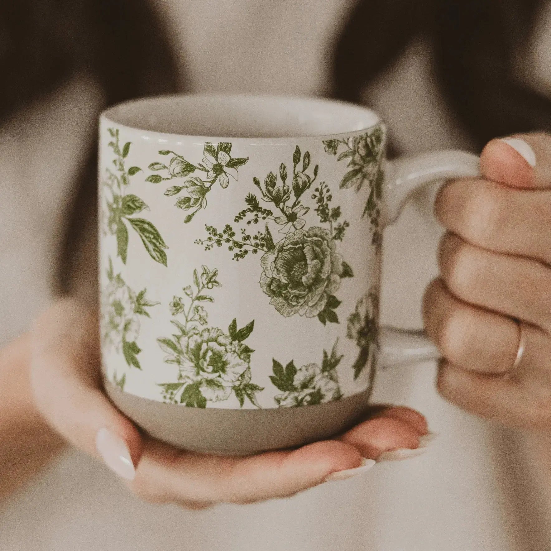 White ceramic mug with green floral print, held gently in hands, perfect for cozy farmhouse decor