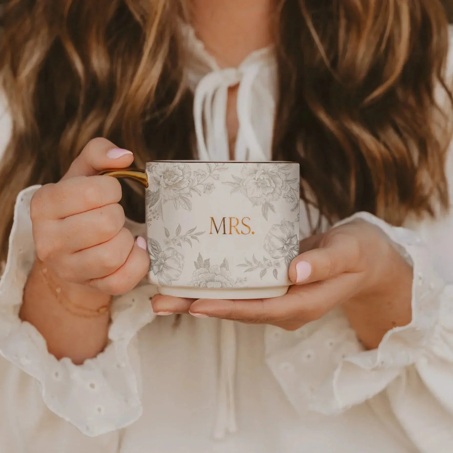 Elegant floral mug with 'MRS.' in gold, held by woman in cozy white blouse, perfect for farmhouse home decor.