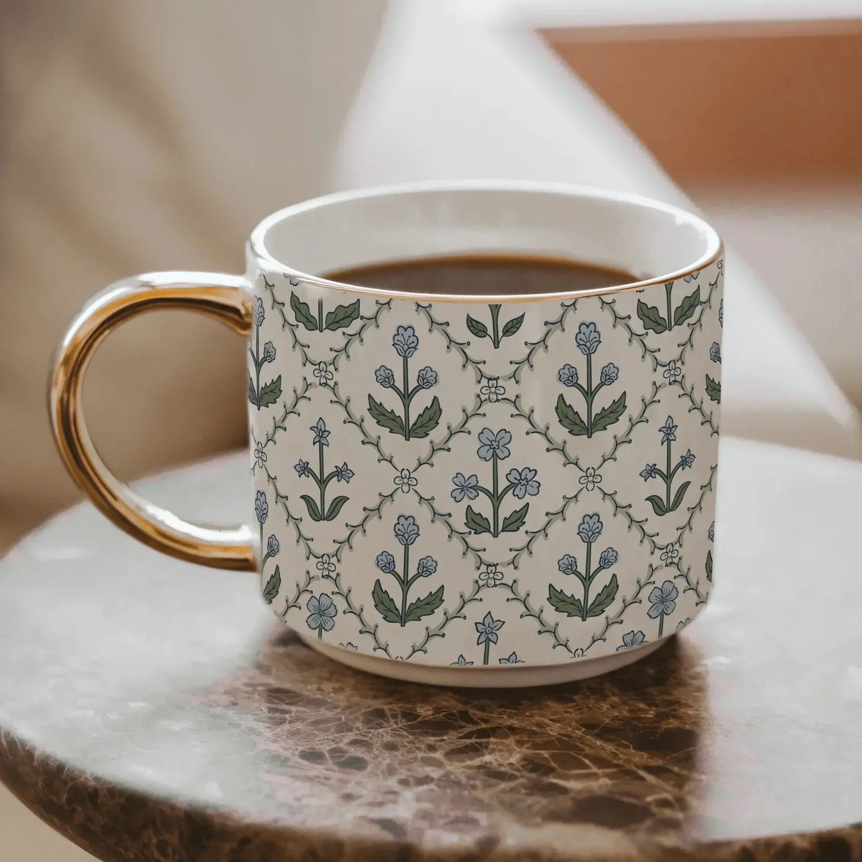 Floral patterned ceramic mug with gold handle, filled with coffee, on marble table, cozy farmhouse decor