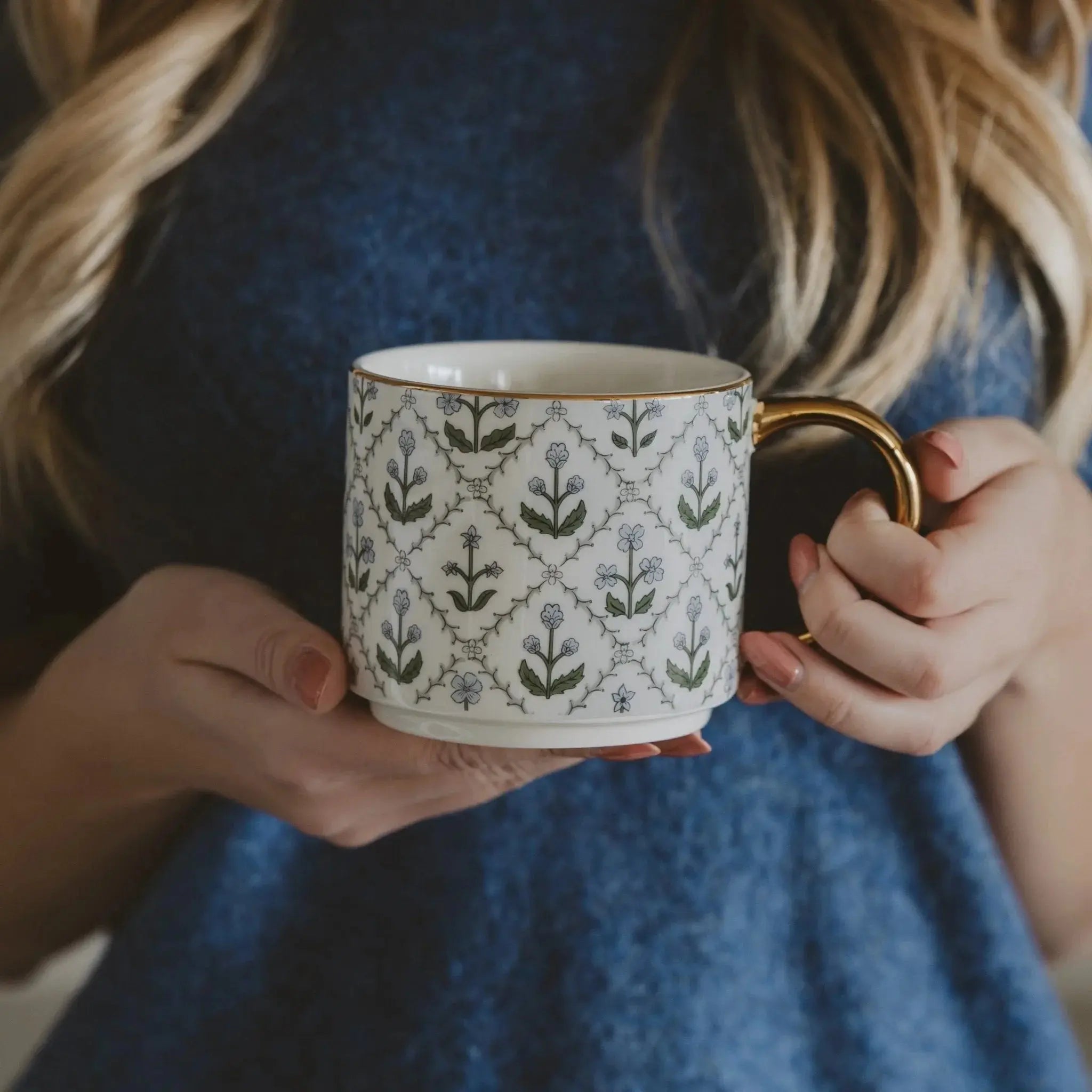 Floral patterned ceramic mug with gold handle, held by woman in cozy blue sweater, perfect for farmhouse home decor.