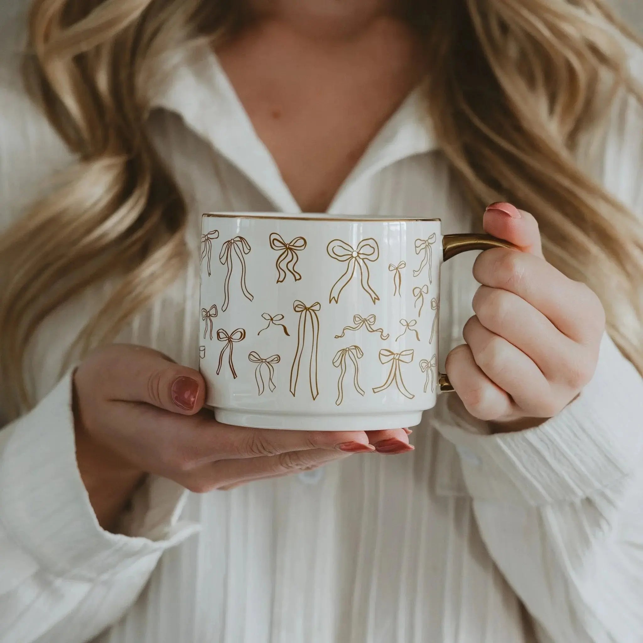 White ceramic mug with gold bow pattern, held by woman in cozy white shirt, farmhouse decor style