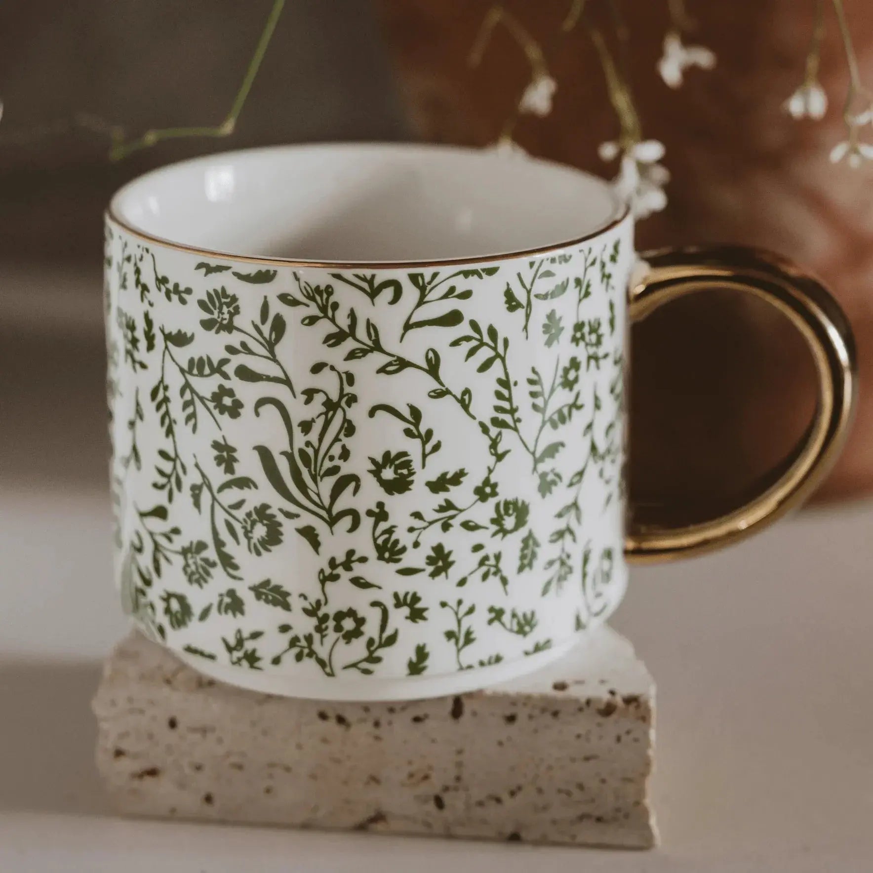 White ceramic mug with green floral pattern and gold rim, cozy farmhouse decor style