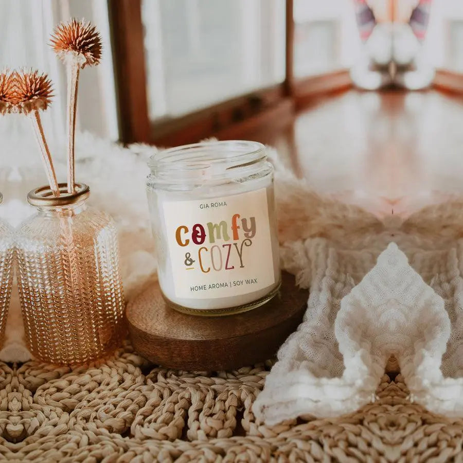 Candle labeled 'comfy & cozy' on a textured surface with decorative elements.