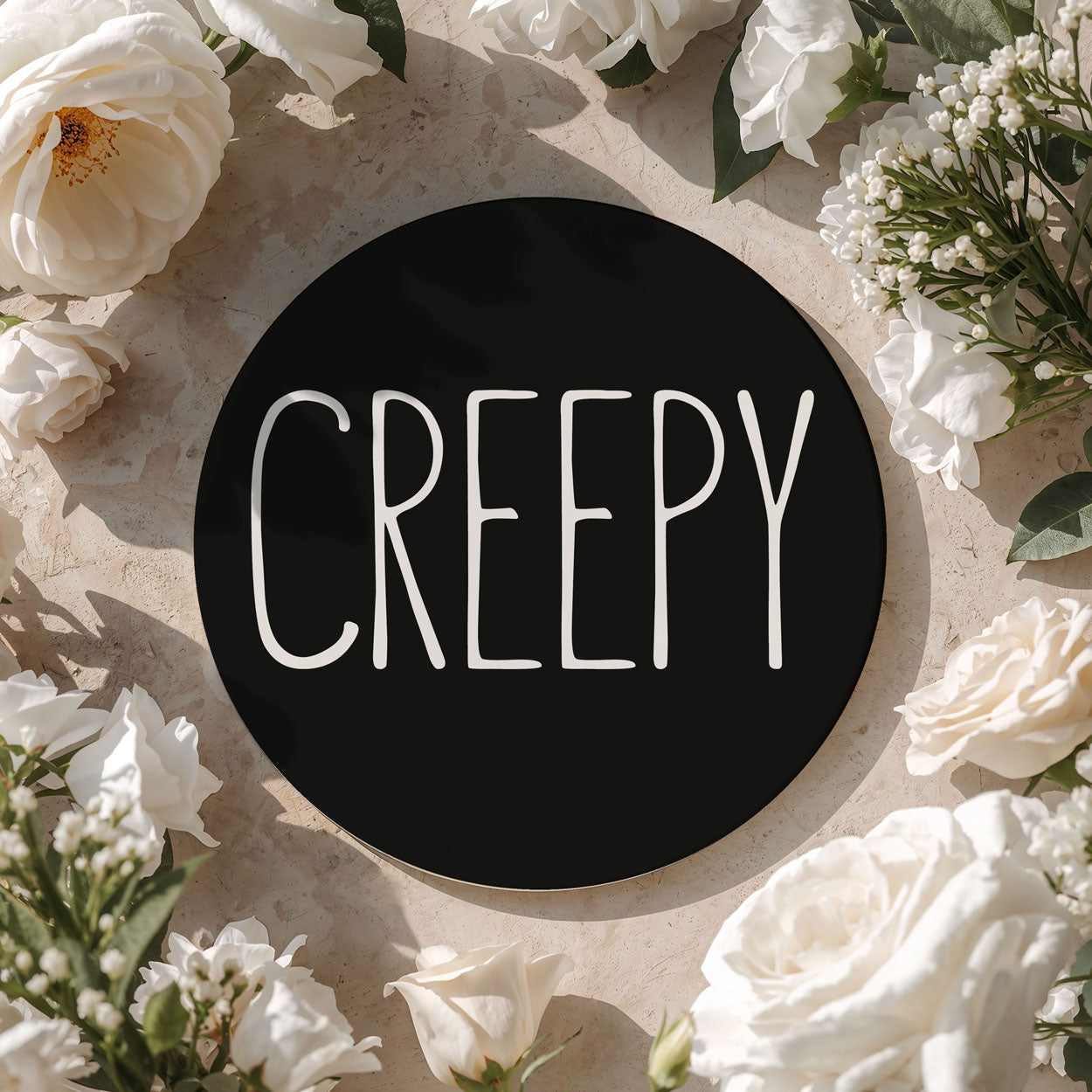 Black circle with 'CREepy' text surrounded by white flowers on a beige background