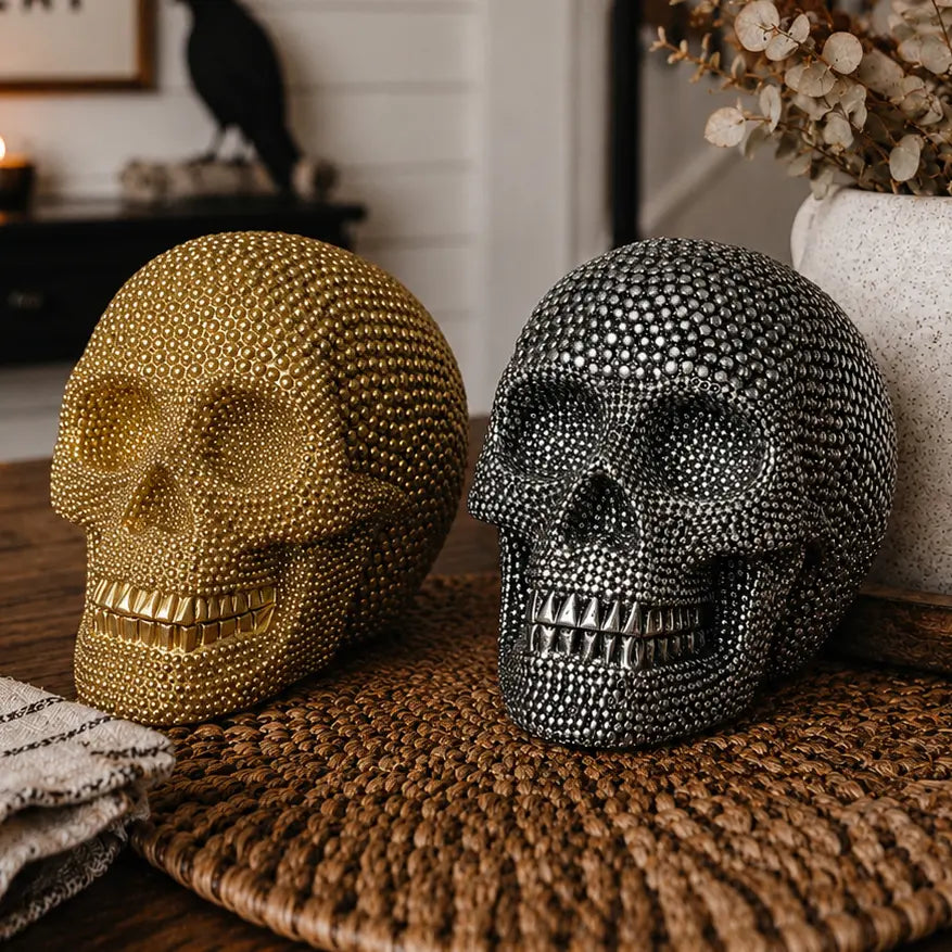 Decorative gold and silver skull sculptures on a woven mat with Halloween decorations in the background.