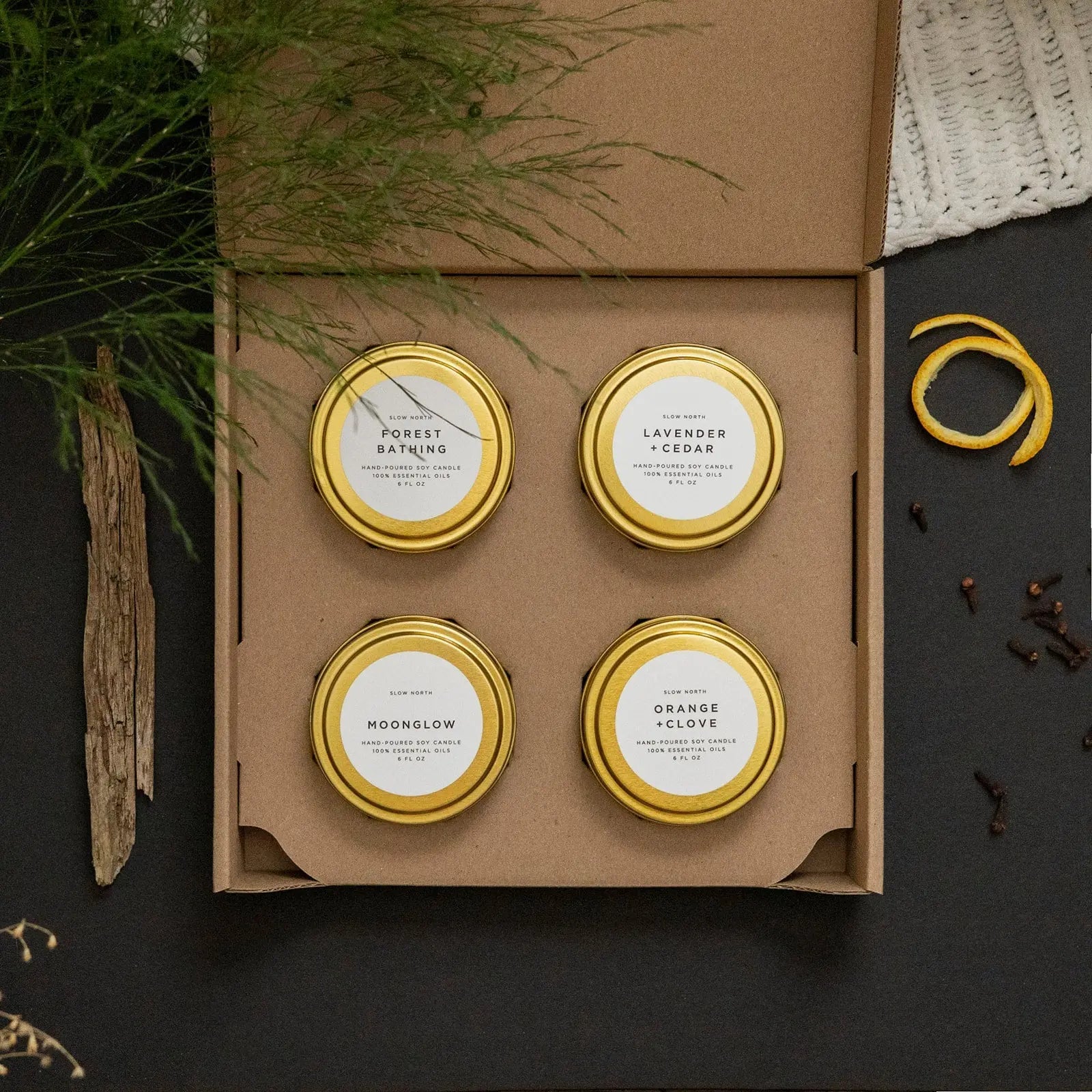 Set of four hand-poured soy candles in gold tins, featuring forest bathing, lavender + cedar, moonglow, and orange + clove scents