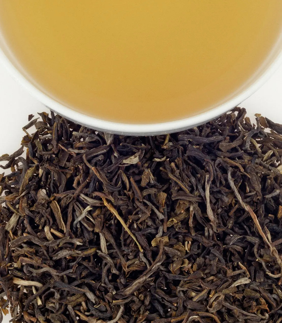 Dry black tea leaves with a cup of brewed tea in the background