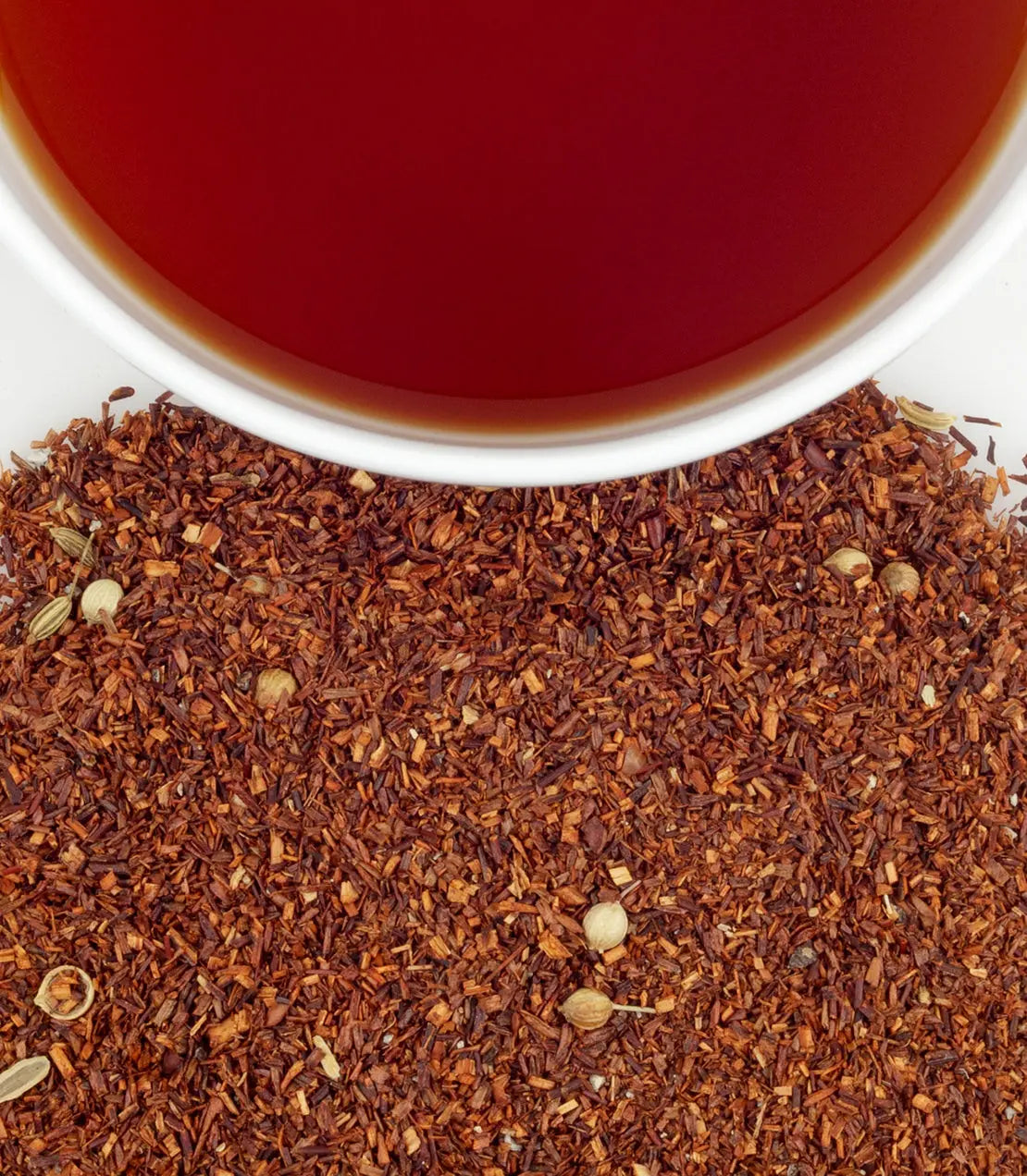Close-up of dried rooibos tea leaves with a cup of red tea in the background.