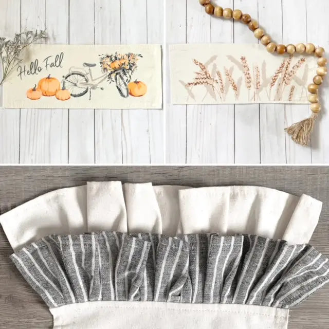Two rectangular fabric fall-themed runner napkins are shown on a whitewashed wood background, with a folded matching napkin below. The top napkin has a bicycle with flowers, pumpkins, and the words 'Hello Fall.