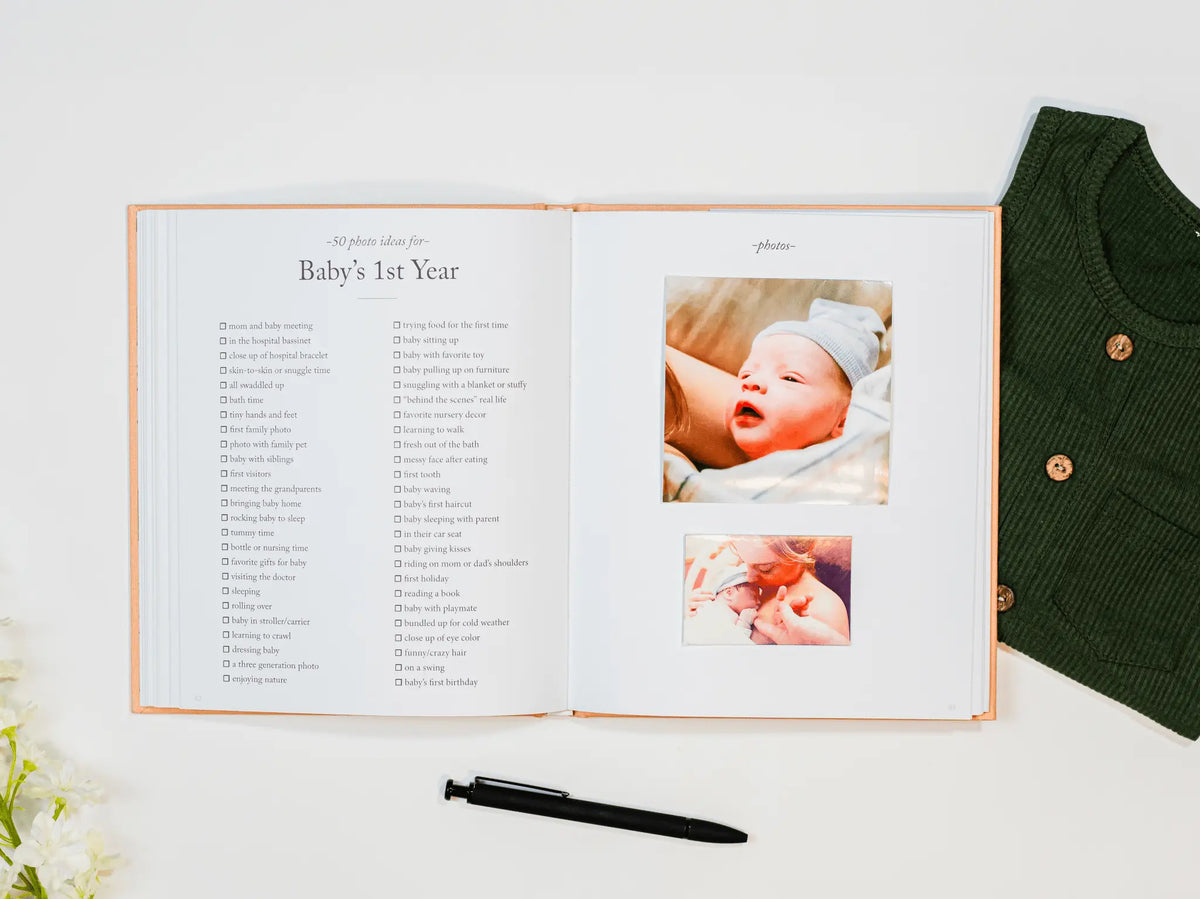 Open photo album with baby milestone photos and text, next to a green knitted sweater.