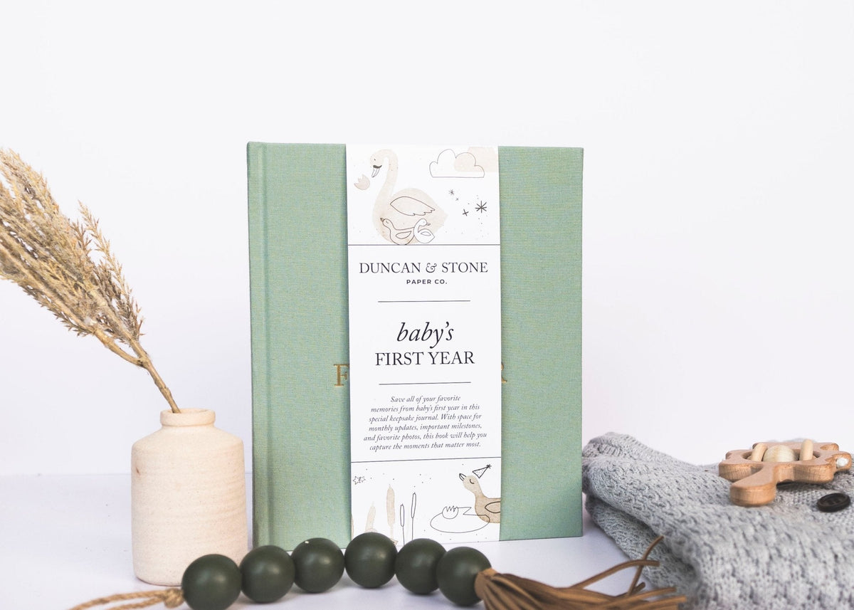 Journal titled 'Baby's First Year' by Duncan & Stone on a white surface with decorative elements.